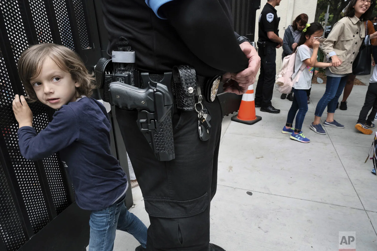 Julian Richner, 9, leaves school for the day to meet his mother as he passes behind an armed security guard at Beverly Hills Unified School District's K-8 Horace Mann School in Beverly Hills, Calif. on Monday, May 13, 2019. Districts nationwide are employing a multi-layered approach for safety that combines mental health programs, bullying prevention initiatives with hardware and software technology, as well as armed and unarmed security officers. (AP Photo/Richard Vogel)