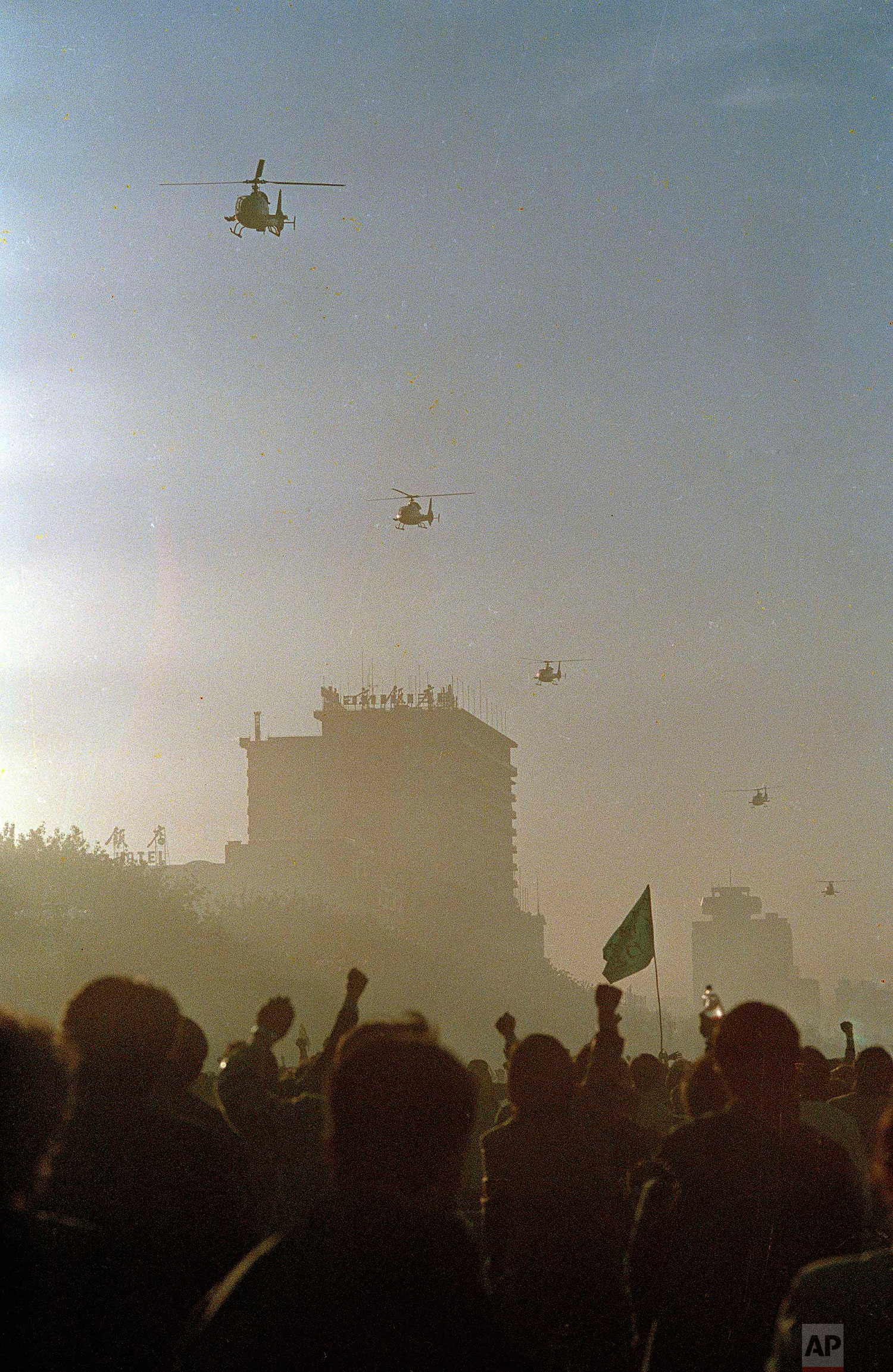  Beijing university students wave fists and flags as five Chinese military helicopters buzz Tiananmen Square at dawn, May 21, 1989. Students have occupied the square for more than a week resulting in the declaration of martial law by Chinese authorit