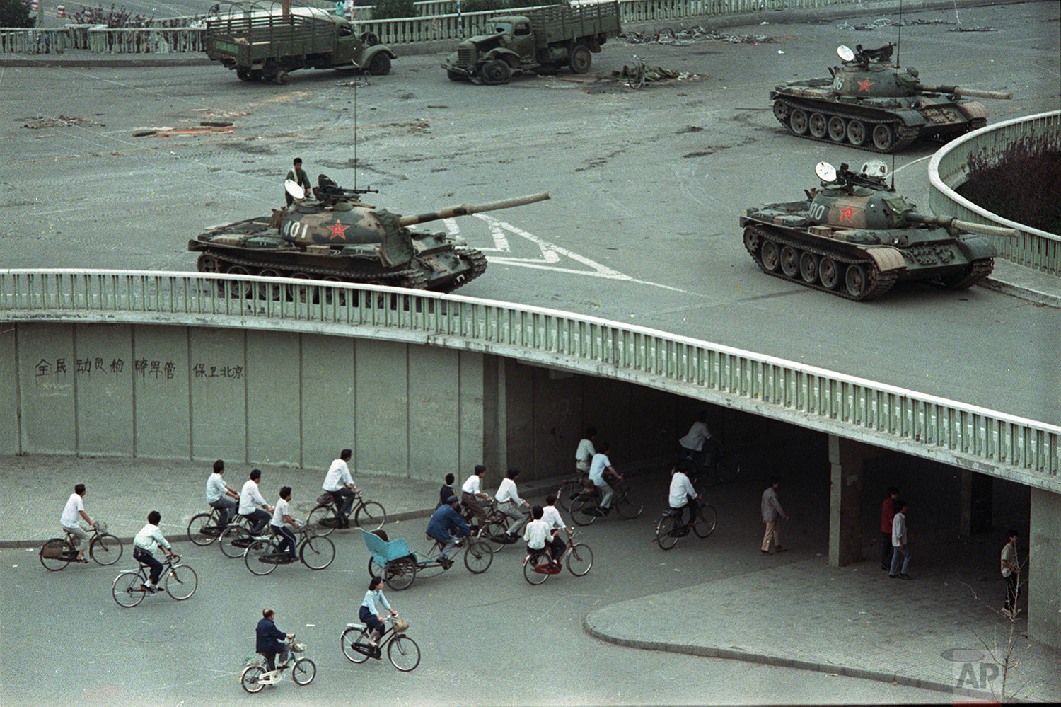  Bicycle commuters, sparse in numbers, pass through a tunnel as above on the overpass military tanks are positioned in Beijing, China, two days after the Tiananmen Square massacre,on Tuesday morning, June 6, 1989.  The slogan on the wall at left read