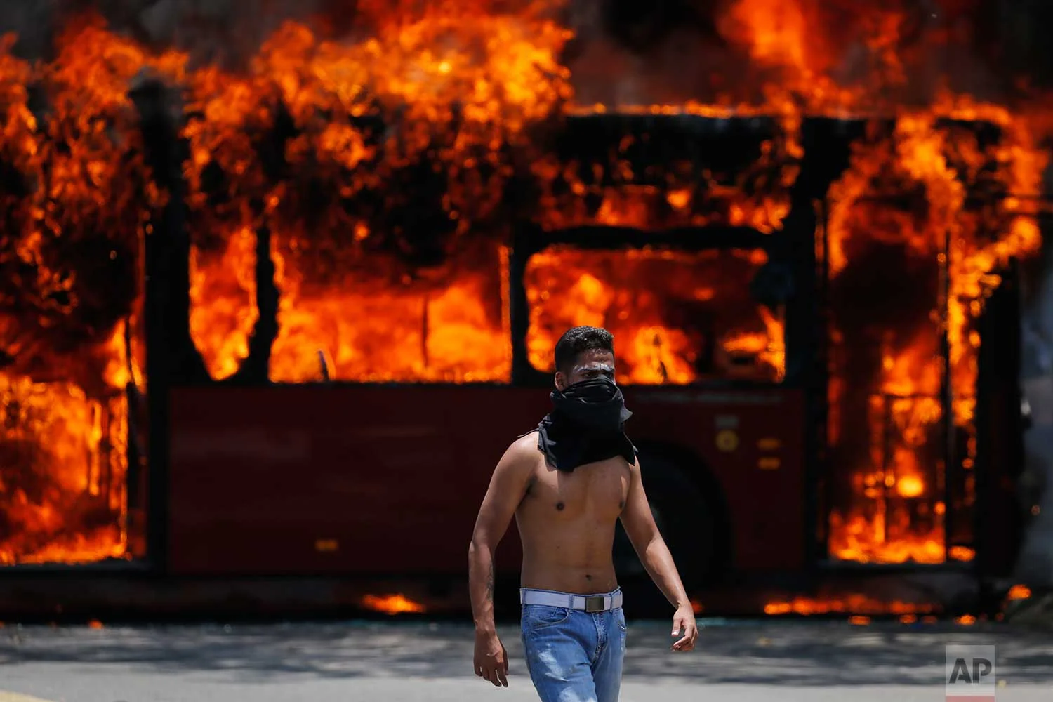 An anti-government protester walks near a bus that was set on fire by opponents of Venezuela's President Nicolas Maduro during clashes between rebel and loyalist soldiers in Caracas, Venezuela, Tuesday, April 30, 2019. Venezuelan opposition leader Juan Guaido took to the streets with a small contingent of heavily armed troops early Tuesday in a bold and risky call for the military to rise up and oust Maduro. (AP Photo/Fernando Llano)