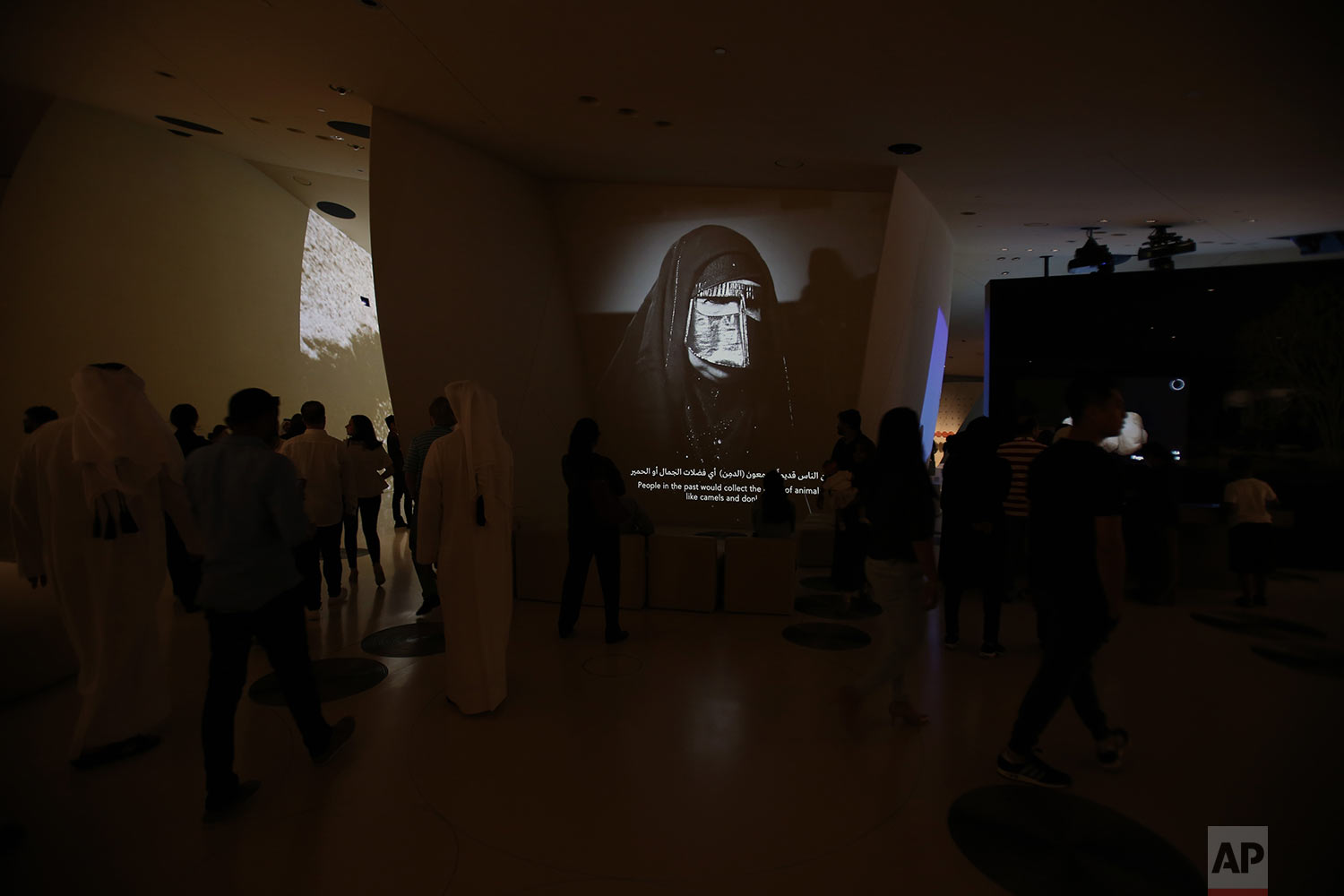  In this Monday, April 22, 2019 photo, people visit one of the galleries with an image of a Qatari woman covered her face with traditional Burqa, at the National Museum of Qatar designed by French architect, Jean Nouvel who got his inspiration from t