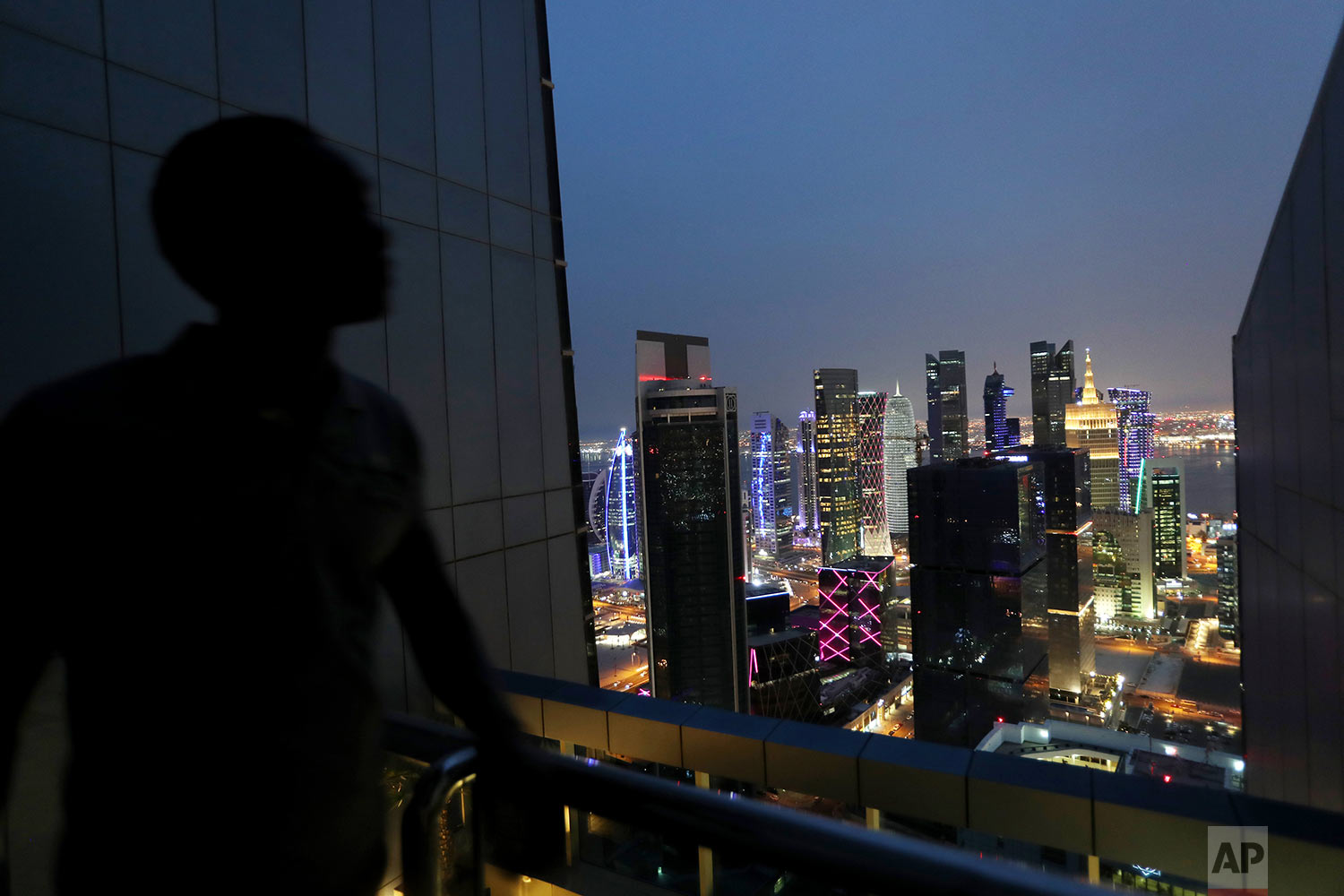  In this Saturday, May 4, 2019 photo, a life guard of a hotel swimming pool watches the night view of West Bay district which is the location of many modern high rises in Doha, Qatar. (AP Photo/Kamran Jebreili) 