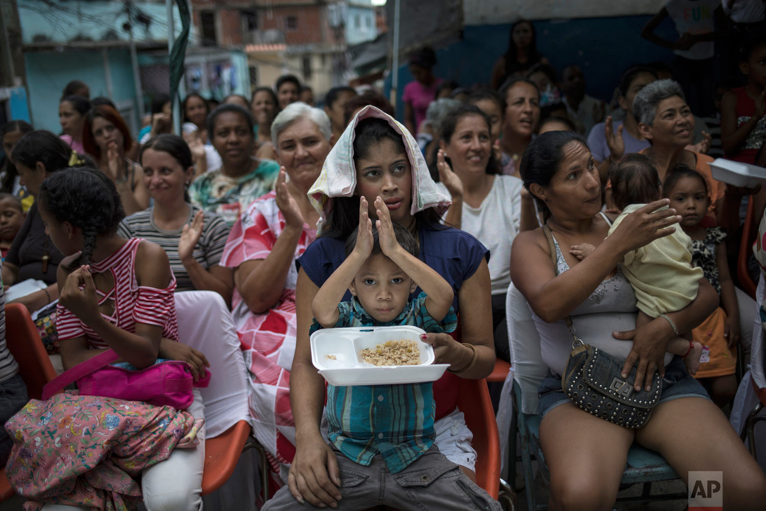Women watch mariachis musicians perform during a Mother's Day block party in Caracas, Venezuela, late Sunday, May 19, 2019. (AP Photo/Rodrigo Abd)