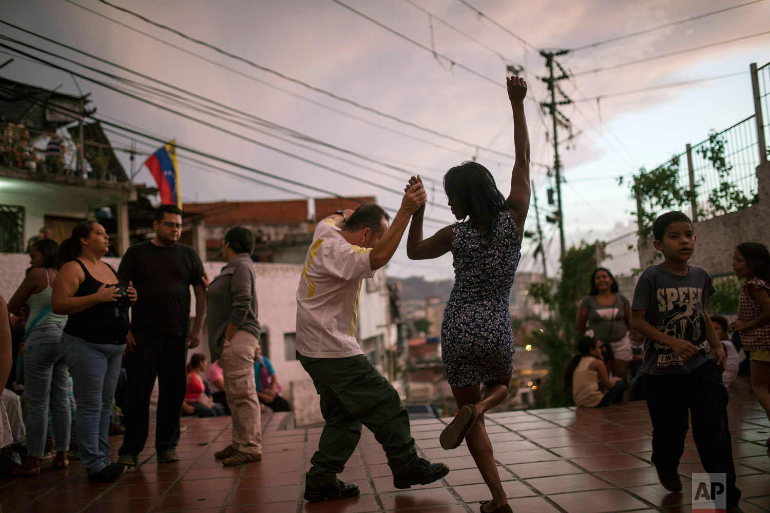 Irene Vaamondez, right, dances with a neighbor as musicians play live music at a public plaza where neighbors socialize in Caracas, Venezuela, at sunset Saturday, May 11, 2019. (AP Photo/Rodrigo Abd)