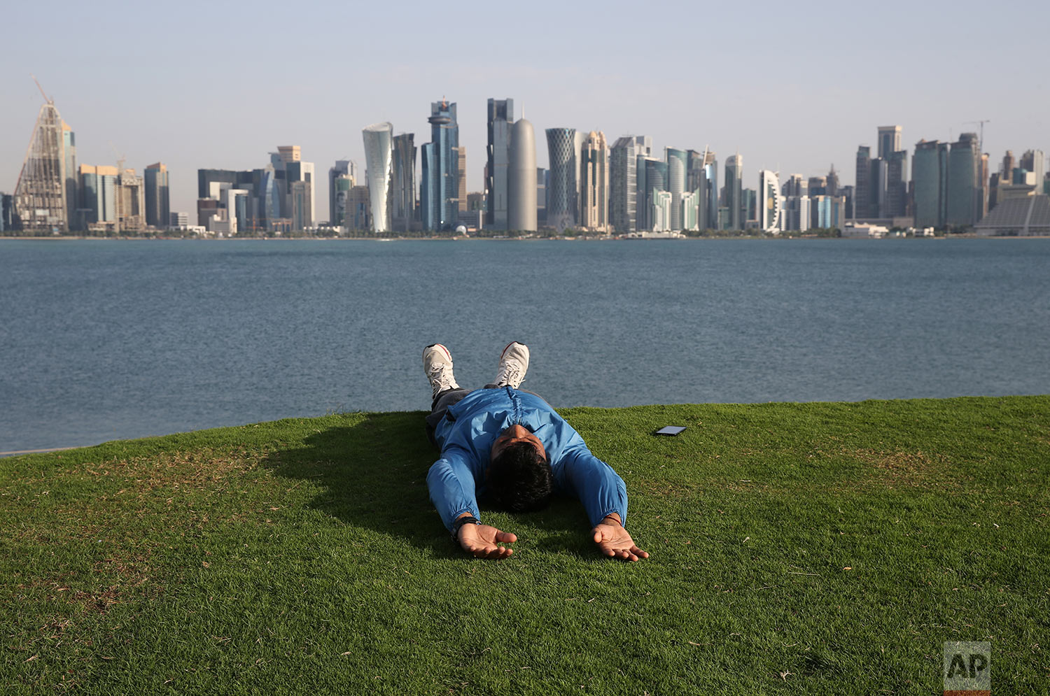  In this Friday, April 19, 2019 photo, a man takes a relax moment on a grass covered hill at the MIA park, overlooking to the skyline of Doha, Qatar. (AP Photo/Kamran Jebreili) 