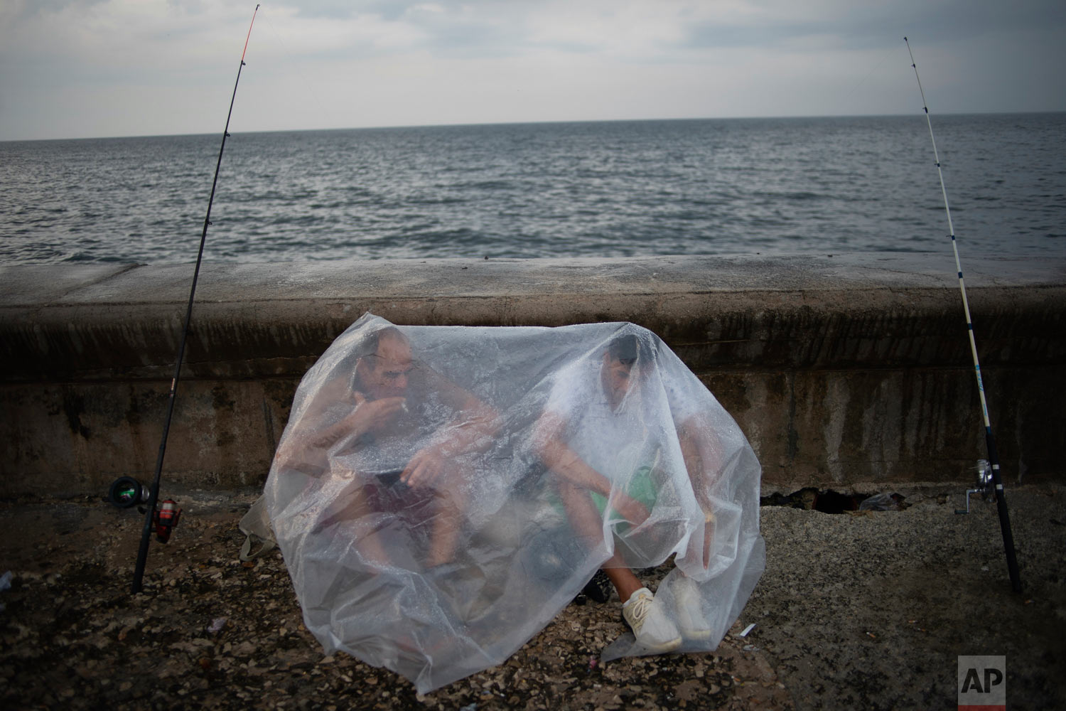  Engelbert Cañete, left, and his friend Ethian Jesus, protect themselves from the rain with a plastic sheet while waiting for the rain to stop so they can continue fishing at the malecón in Havana, Cuba, Monday, May 6, 2019. (AP Photo/Ramon Espinosa)