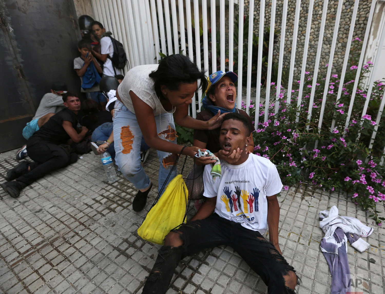 An anti-government protester calls for help as she and another woman help a fellow demonstrator who is overcome by teargas during clashes with security forces in Caracas, Venezuela, Wednesday, May 1, 2019. Opposition leader Juan Guaidó called for Venezuelans to fill streets around the country to demand President Nicolás Maduro's ouster. (AP Photo/Fernando Llano)