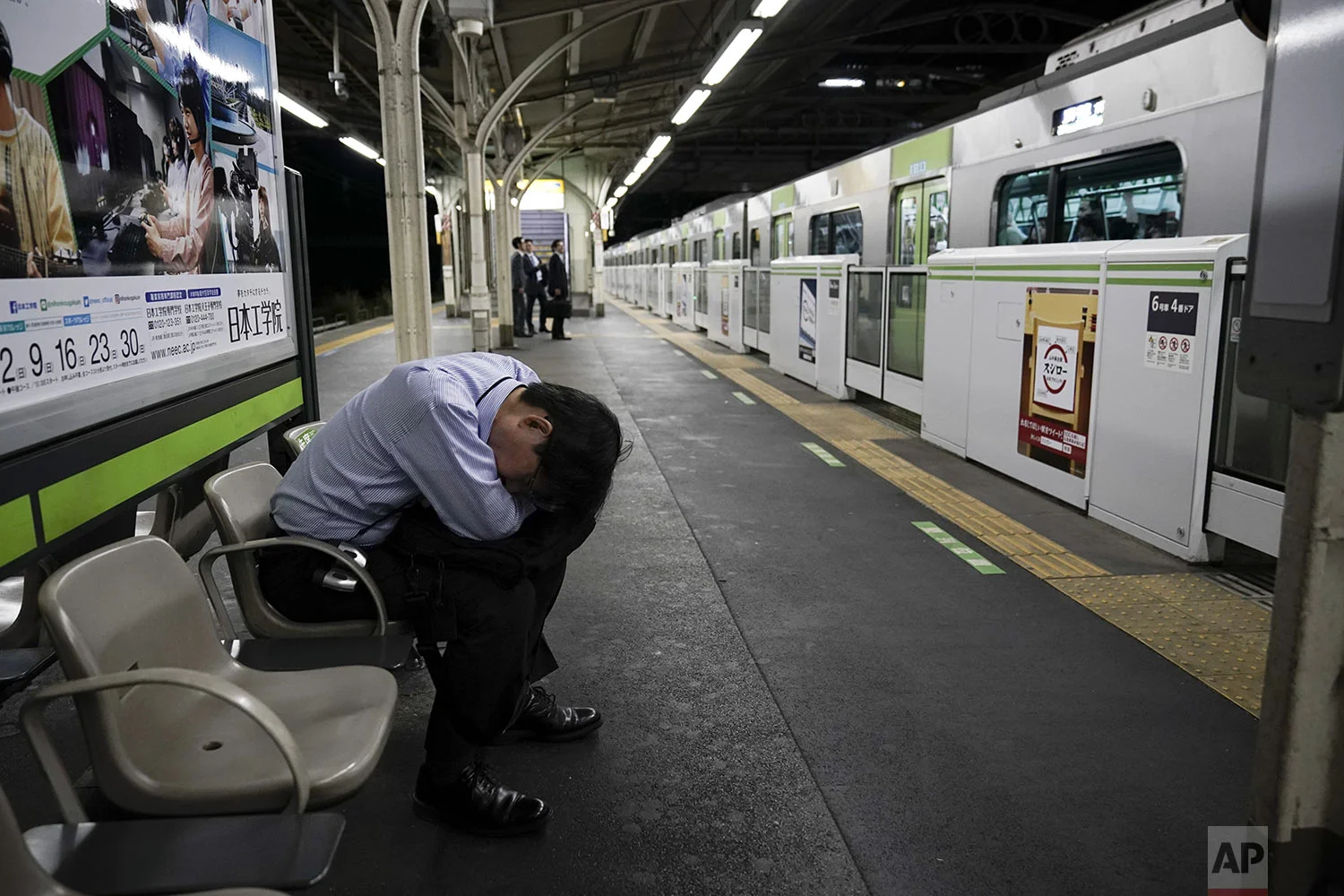 A commuter falls asleep on a platform as a Yamanote Line train departs in Tokyo, Saturday, May 25, 2019. (AP Photo/Jae C. Hong)