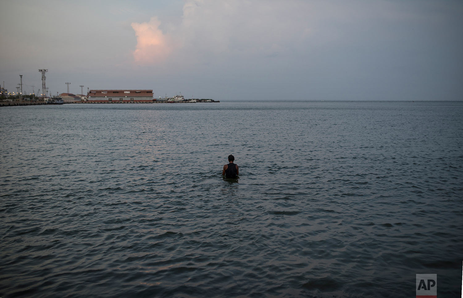 In this May 14, 2019 photo, Raul Navas, 25, bathes in Maracaibo Lake after a day of work a the flea market in Maracaibo, Venezuela. (AP Photo/Rodrigo Abd)