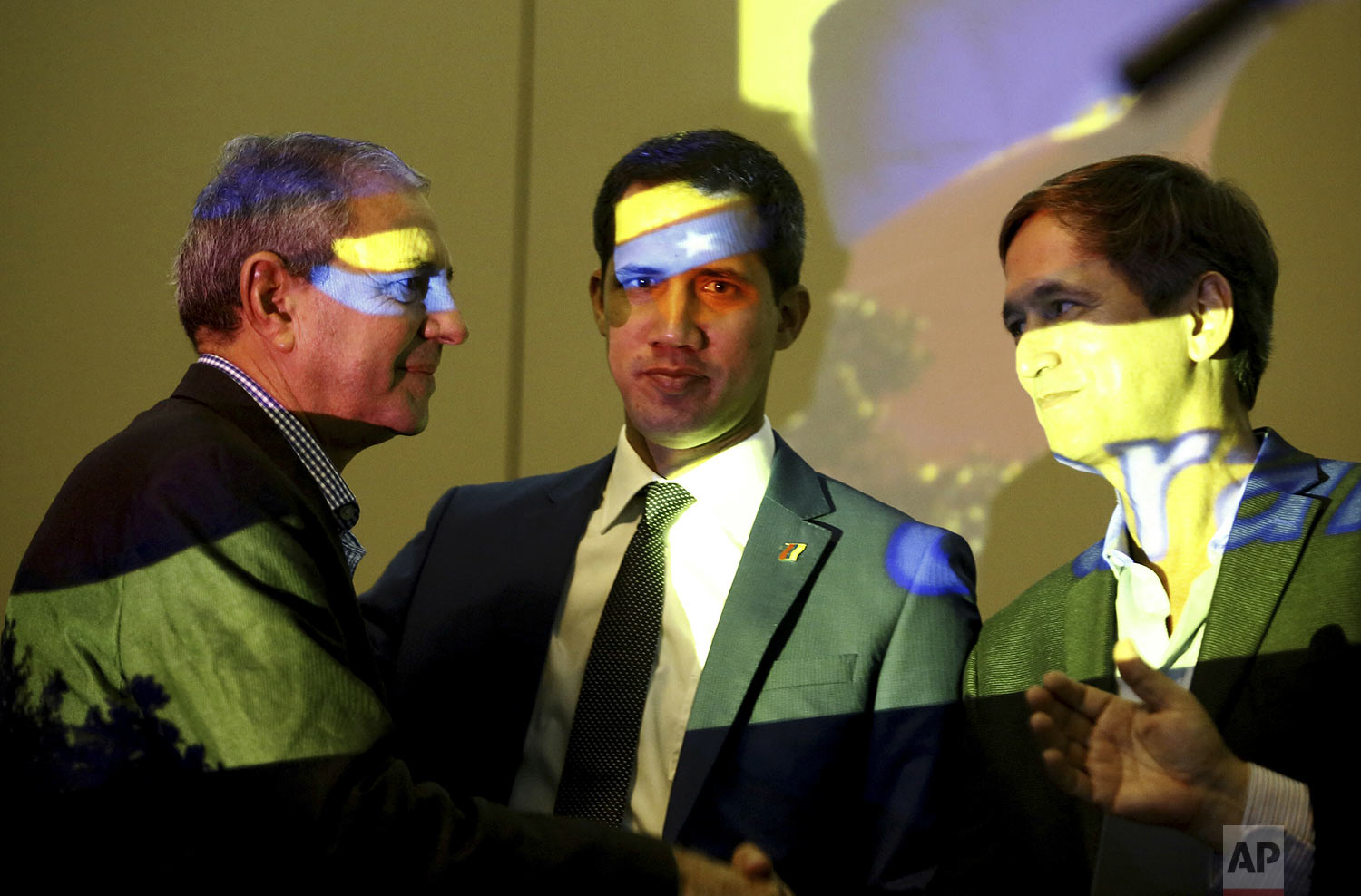 Venezuela's opposition leader and self-proclaimed interim president Juan Guaido, center, speaks with members of the opposition in Carabobo State, Manuel Barreto, left, and Lucio Herrera, prior a speech during a meeting with supporters, at a hotel in Valencia, Venezuela, June 7, 2019. The colors on their faces are the colors of Venezuelan flag projected by a data projector. (AP Photo/Juan Carlos Hernandez)