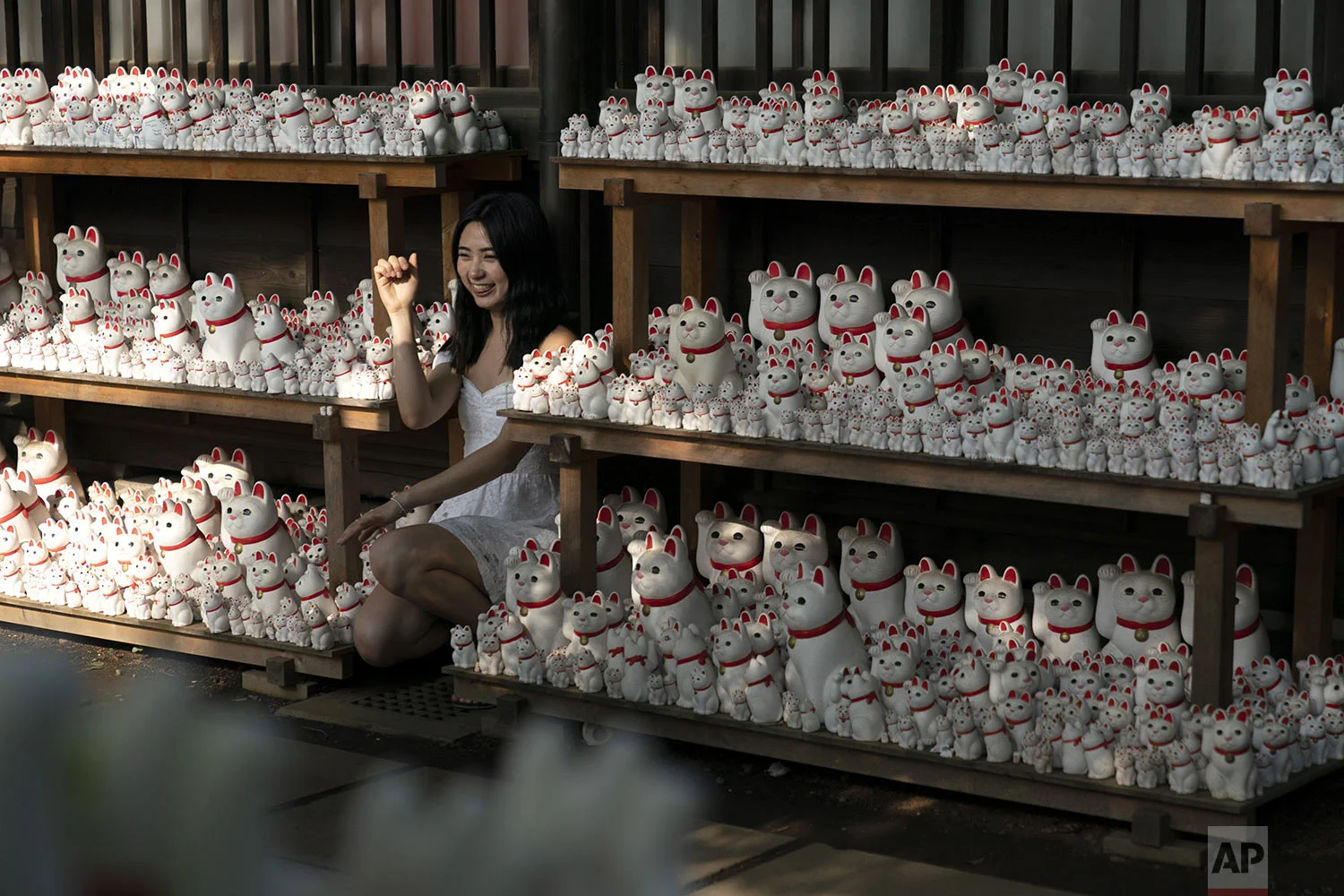 A woman poses for photos with beckoning cat figurines at Gotokuji Temple in Tokyo, Tuesday, June 25, 2019. (AP Photo/Jae C. Hong)