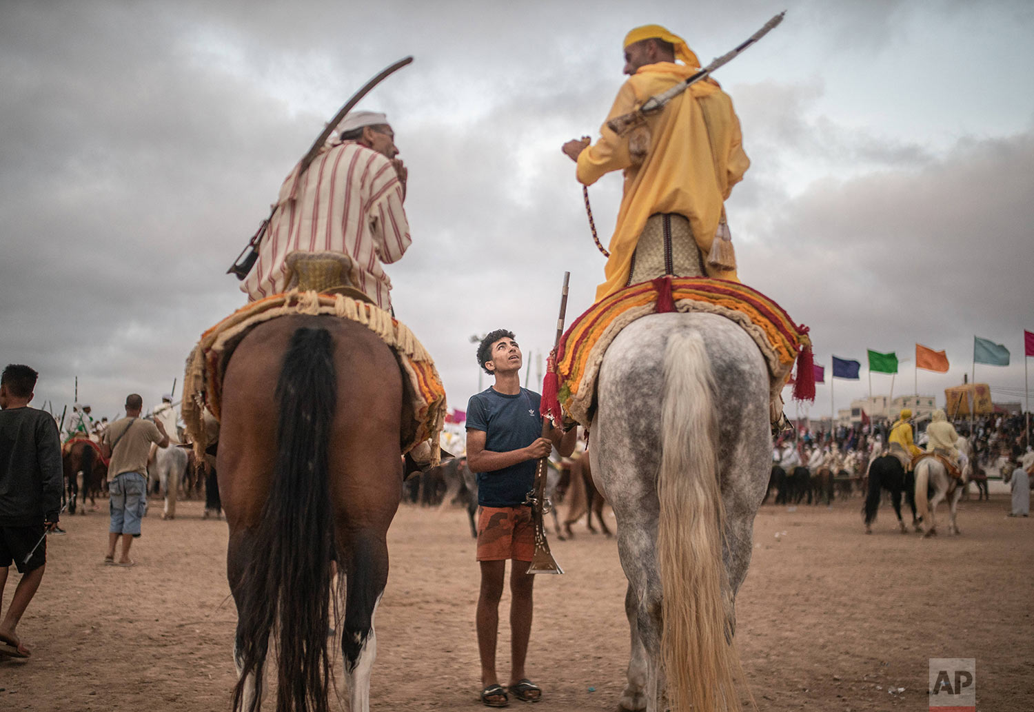 A boy hands a file to horse riders waiting for their turn to take part in an equestrian show known as Fantasia or Tabourida, in the coastal town of El Jadida, Morocco, July 25, 2019. (AP Photo/Mosa'ab Elshamy)
