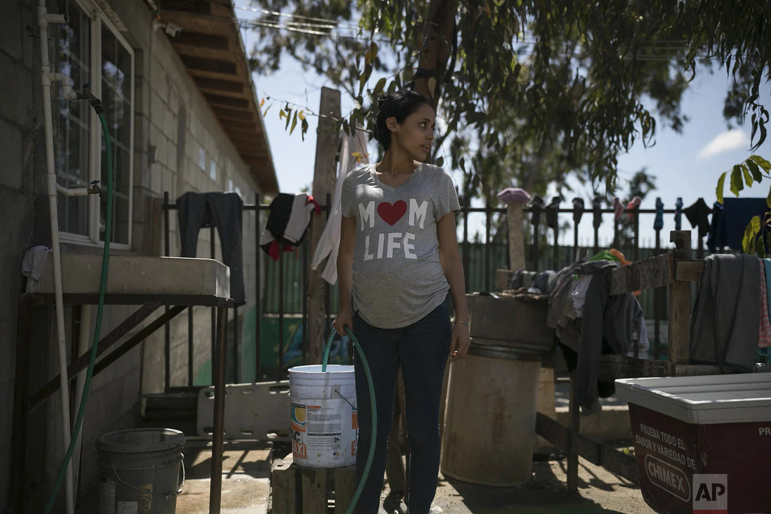 In this May 23, 2019 photo, pregnant teen migrant Milagro de Jesus Henriquez Ayala fills a bucket with water at the Agape World Mission shelter in Tijuana, Mexico. (AP Photo/Emilio Espejel)