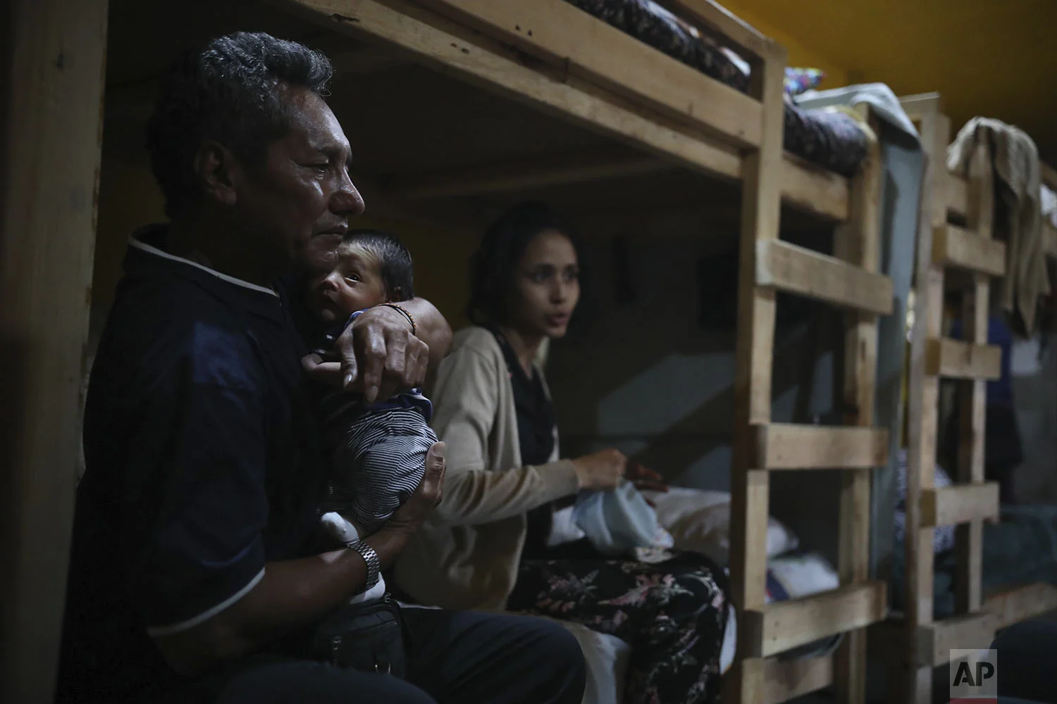 In this June 15, 2019 photo, Manuel Henriquez holds his grandson Alexander, as he sits next to his daughter Milagro de Jesus Henriquez Ayala, on her bed, at the Agape World Mission shelter in Tijuana, Mexico. (AP Photo/ Emilio Espejel)