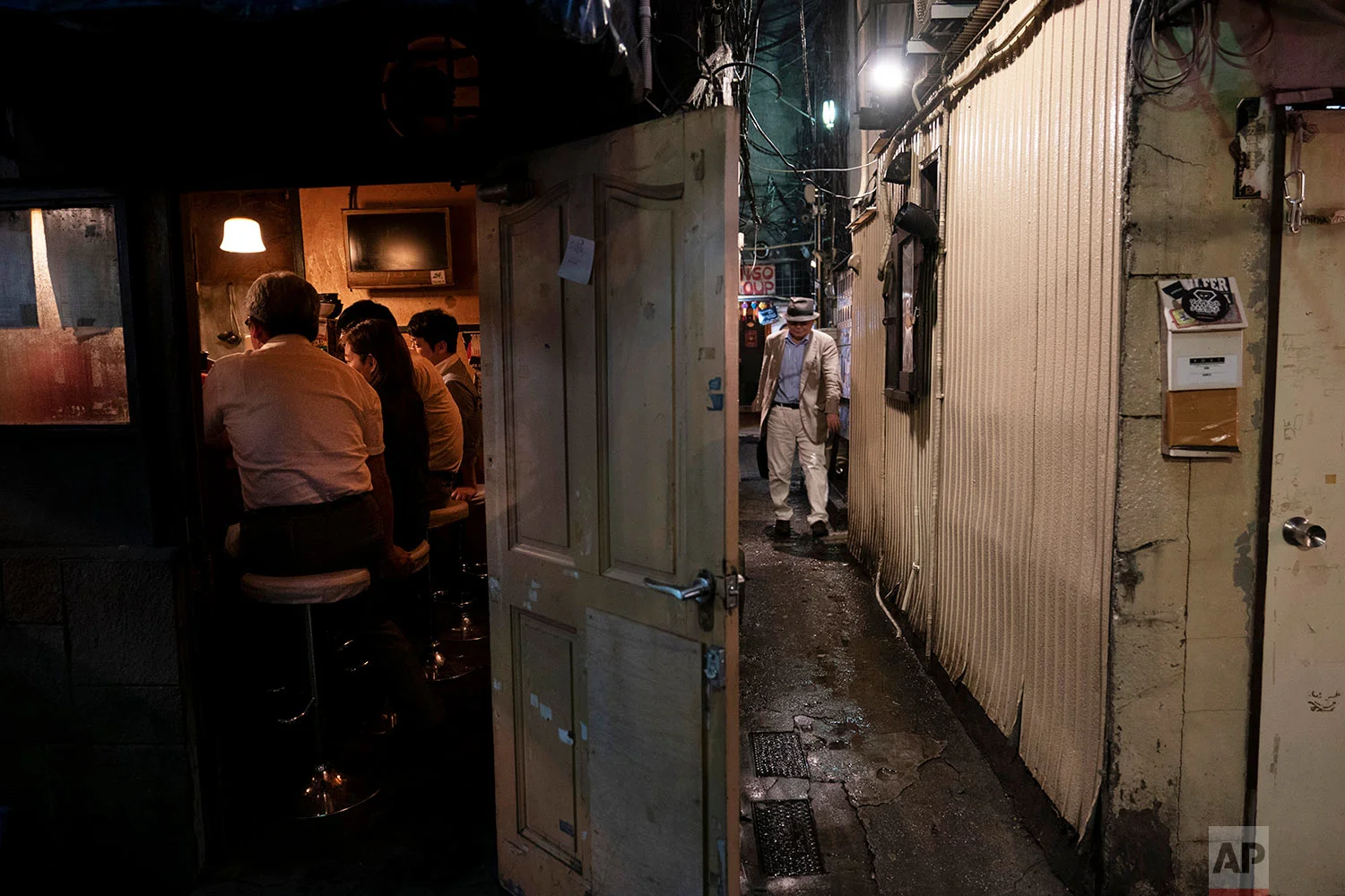 A man makes his way through a narrow passageway between two buildings at the Golden Gai in the Shinjuku district of Tokyo, July 17, 2019. (AP Photo/Jae C. Hong)
