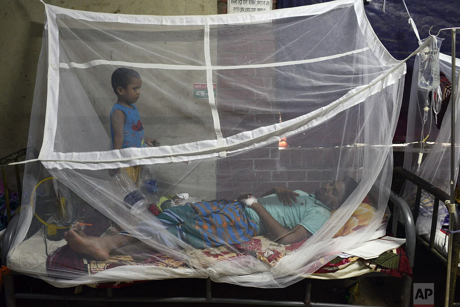 A man receives treatment for dengue, with his son standing beside him, at Shaheed Suhrawardy Medical College and Hospital in Dhaka, Bangladesh, Wednesday, July 31, 2019. (AP Photo/Mahmud Hossain Opu)