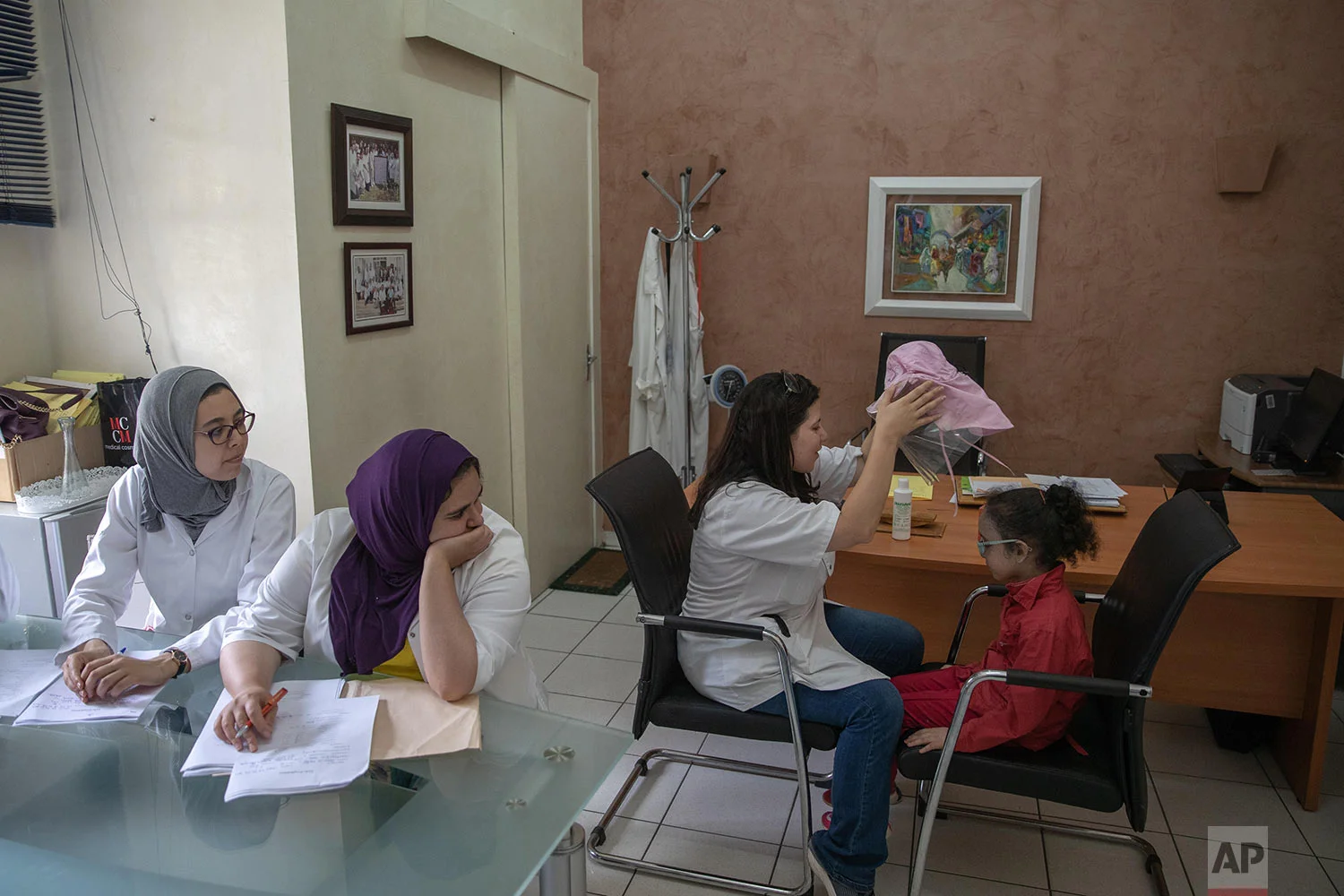 A nurse takes off a protective mask as she performs skin checkups for 6 year old Yasmin, who is affected by a rare disorder called xeroderma pigmentosum, or XP, inside a hospital in Casablanca, Morocco, July 24, 2019. (AP Photo/Mosa'ab Elshamy)