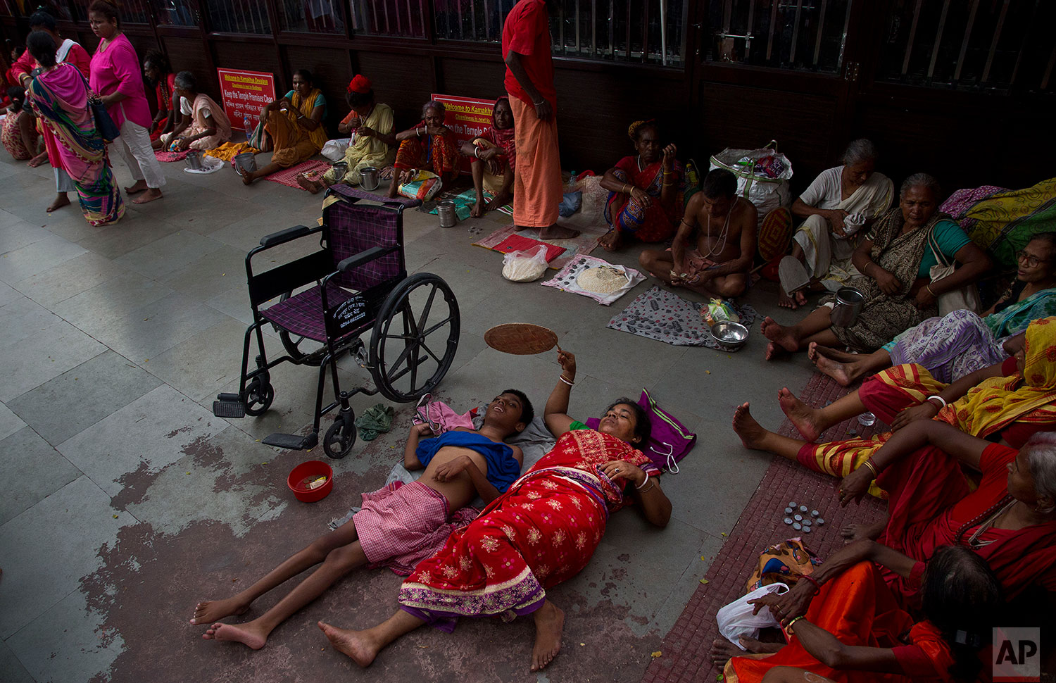 Monika Deb Nath, 45, uses a hand fan and rests on the floor with her son Gopal, 17, at the Kamakhya temple during the Ambubachi festival in Gauhati, India, June 25, 2019 . Monika, 45, and her husband have visited the Kamakhya temple four years in a row for the annual Ambubachi festival, praying for a miracle to heal their son from cerebral palsy, which has left him with almost no control over his own body. The temple is presided over by the goddess Kamakhya, the most important goddess of tantric worship, an esoteric form of Hinduism.(AP Photo/Anupam Nath)