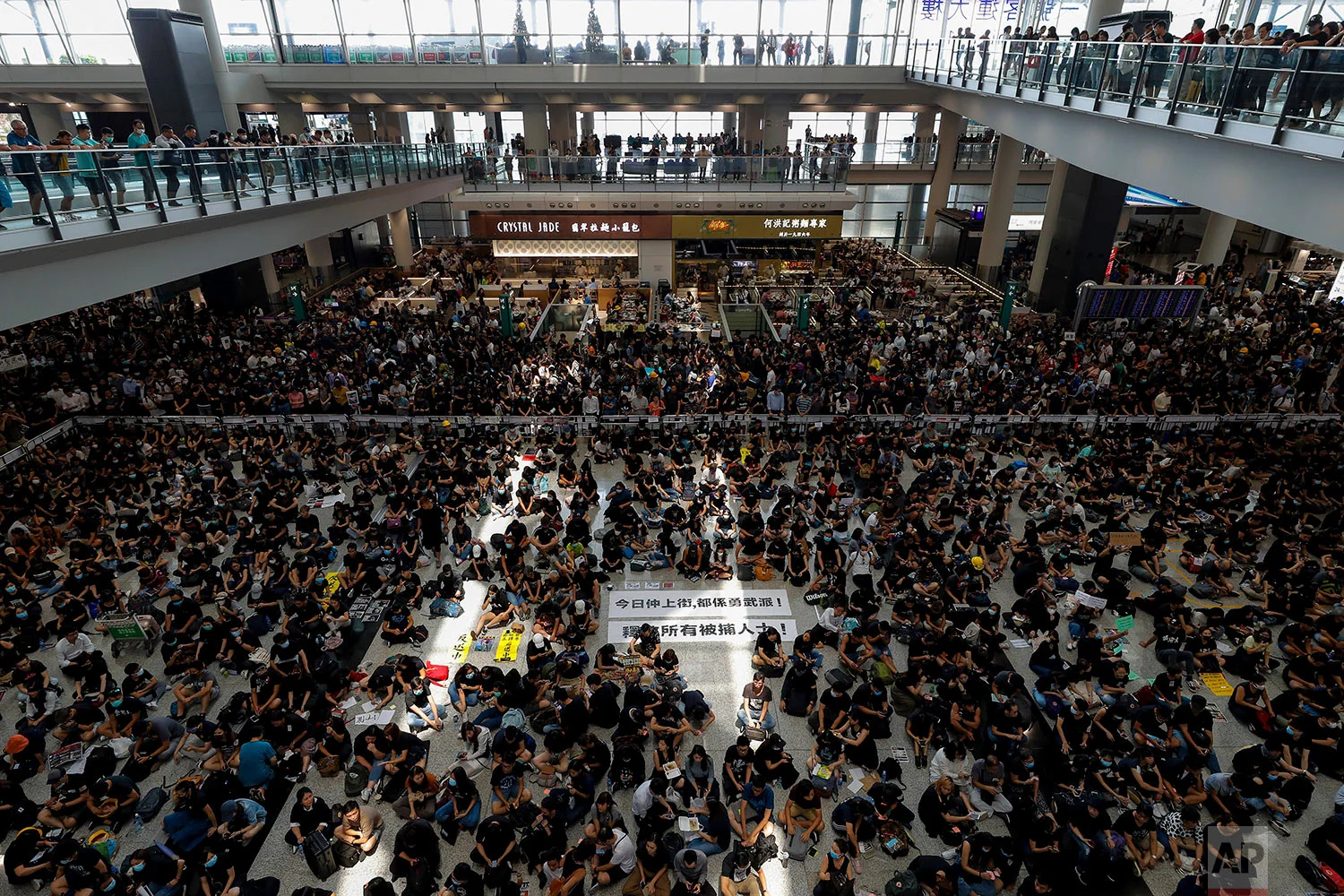 Protesters surround banners that read: "Those on the street today are all warriors!" center top, and "Release all the detainees!" during a sit-in rally at the arrival hall of the Hong Kong International airport in Hong Kong, Aug. 12, 2019. (AP Photo/Vincent Thian)