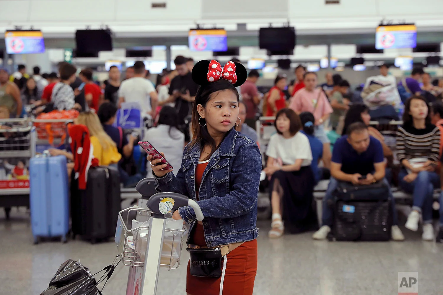 A woman wearing Minnie Mouse headgear looks on as stranded travelers gather near the closed check-in counters at the Airport in Hong Kong, Tuesday, Aug. 13, 2019. (AP Photo/Kin Cheung)