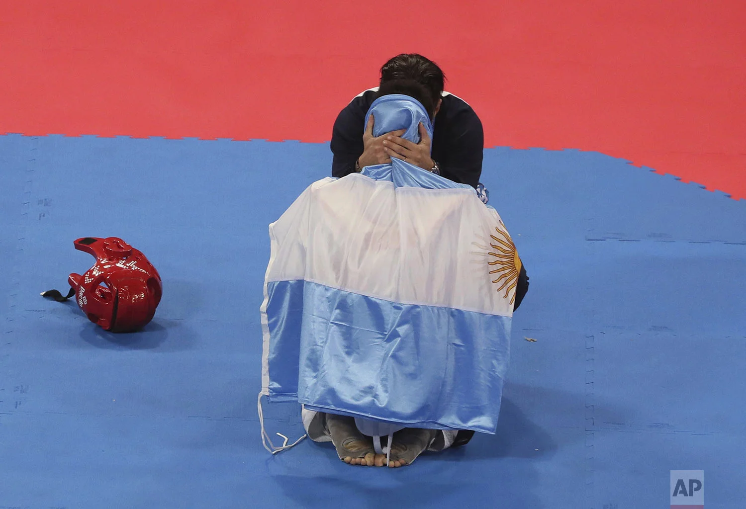Argentina's Lucas Guzman is draped in his nation's flag as he's congratulated by his coach after winning the gold in the men's under 58kg Taekwondo event, after Guzman defeated Brandon Plaza, of Mexico, at the Pan American Games in Lima, Peru, Saturday, July 27, 2019. (AP Photo/Fernando Llano)