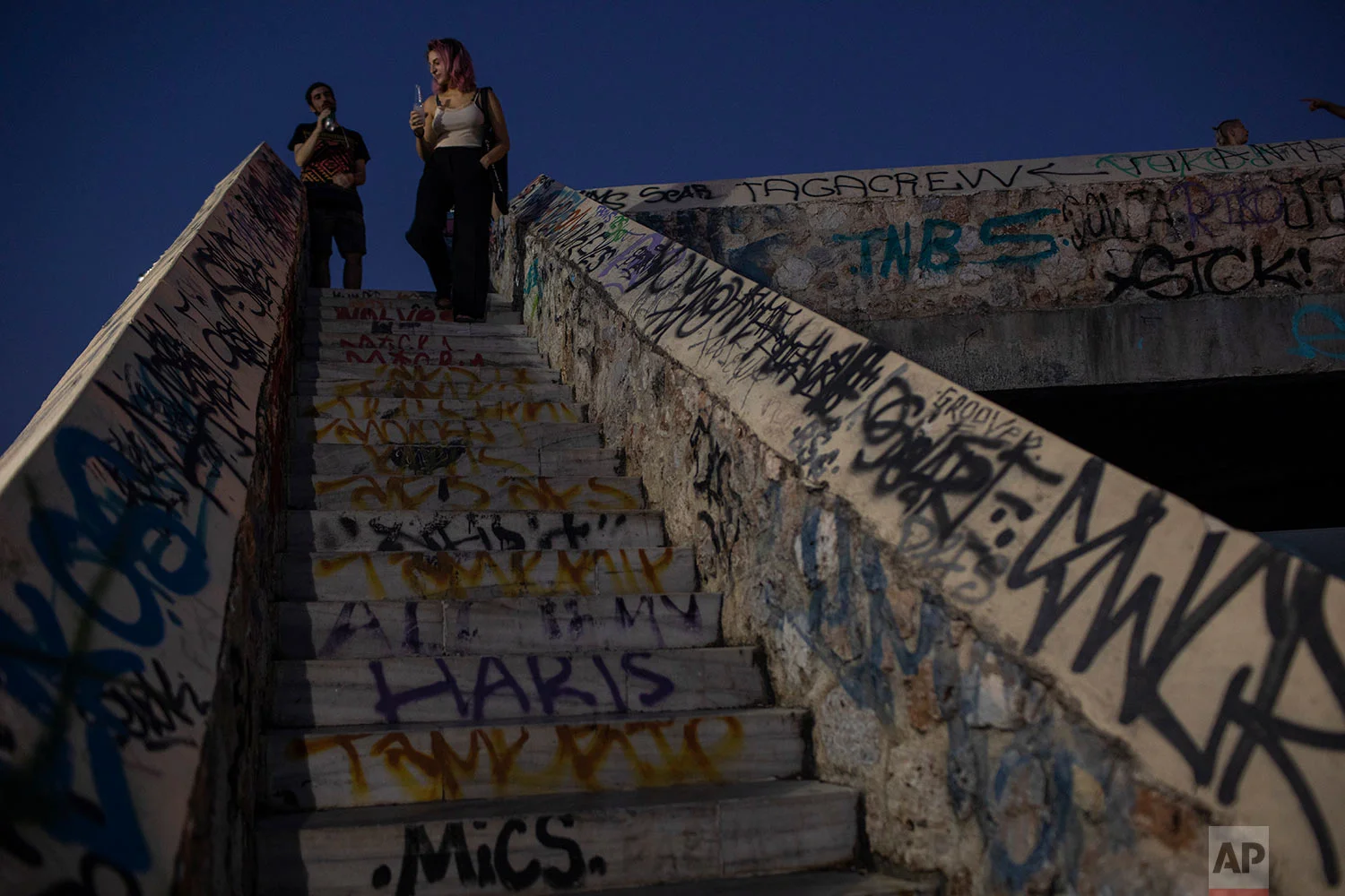 People stand on a graffiti-covered pedestrian bridge over railway lines beside the ancient Kerameikos cemetery in central Athens, July 26, 2019. (AP Photo/Petros Giannakouris)