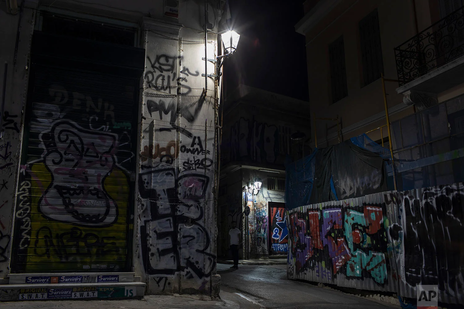 A man stands in a street next a shop and houses covered with graffiti in Athens' Plaka district, July 22, 2019. (AP Photo/Petros Giannakouris)