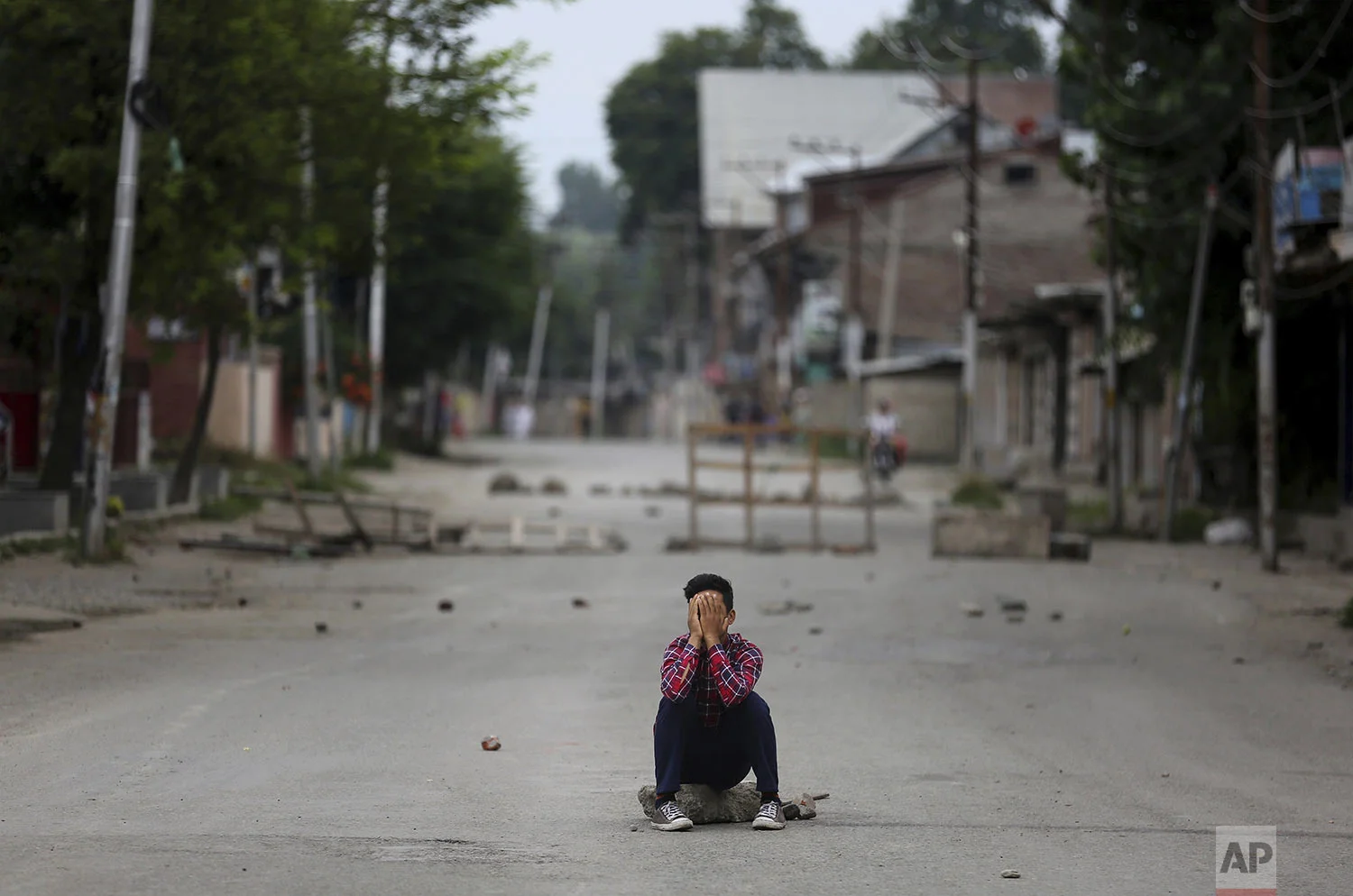 A protester covers his face as he sits on a rock during an anti-India protest in Srinagar, India, Friday, Aug. 9, 2019. (AP Photo/Altaf Qadri)