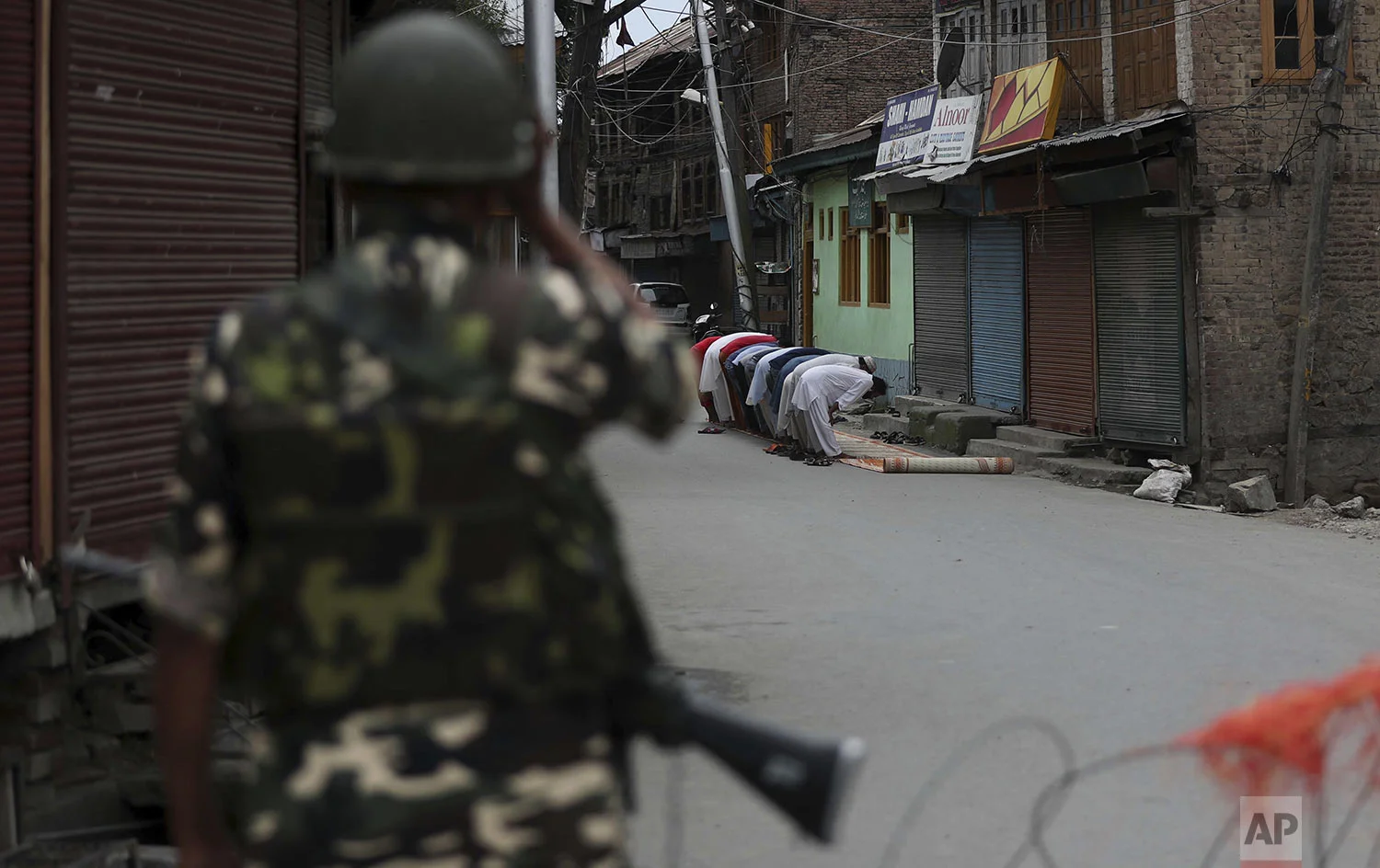 An Indian paramilitary soldier stands guard as Kashmiri Muslims offer Friday prayers on a street outside a local mosque during curfew like restrictions in Srinagar, India, Friday, Aug. 16, 2019. (AP Photo/Mukhtar Khan)