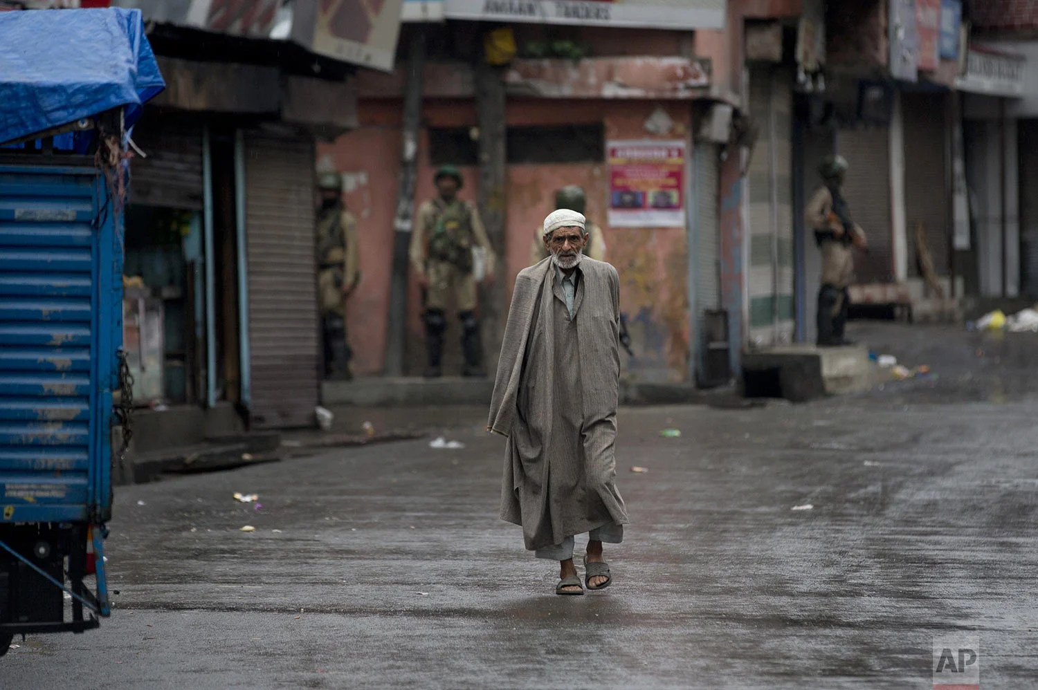 A Kashmiri man walks as Indian paramilitary soldiers stand guard during security lockdown in Srinagar, Indian controlled Kashmir, Wednesday, Aug. 14, 2019. (AP Photo/ Dar Yasin)