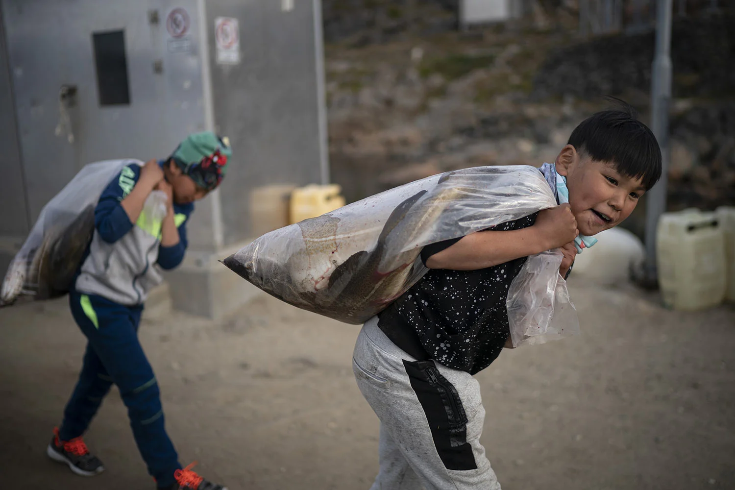 Boys carry plastic bags full of fish on Aug. 15, 2019, in Kulusuk, Greenland. According to local resident Mugu Utuaq, the winter that used to last as long as 10 months when he was a boy can now be as short as five months. Scientists are hard at work in Greenland, trying to understand the alarmingly rapid melting of the ice. (AP Photo/Felipe Dana)