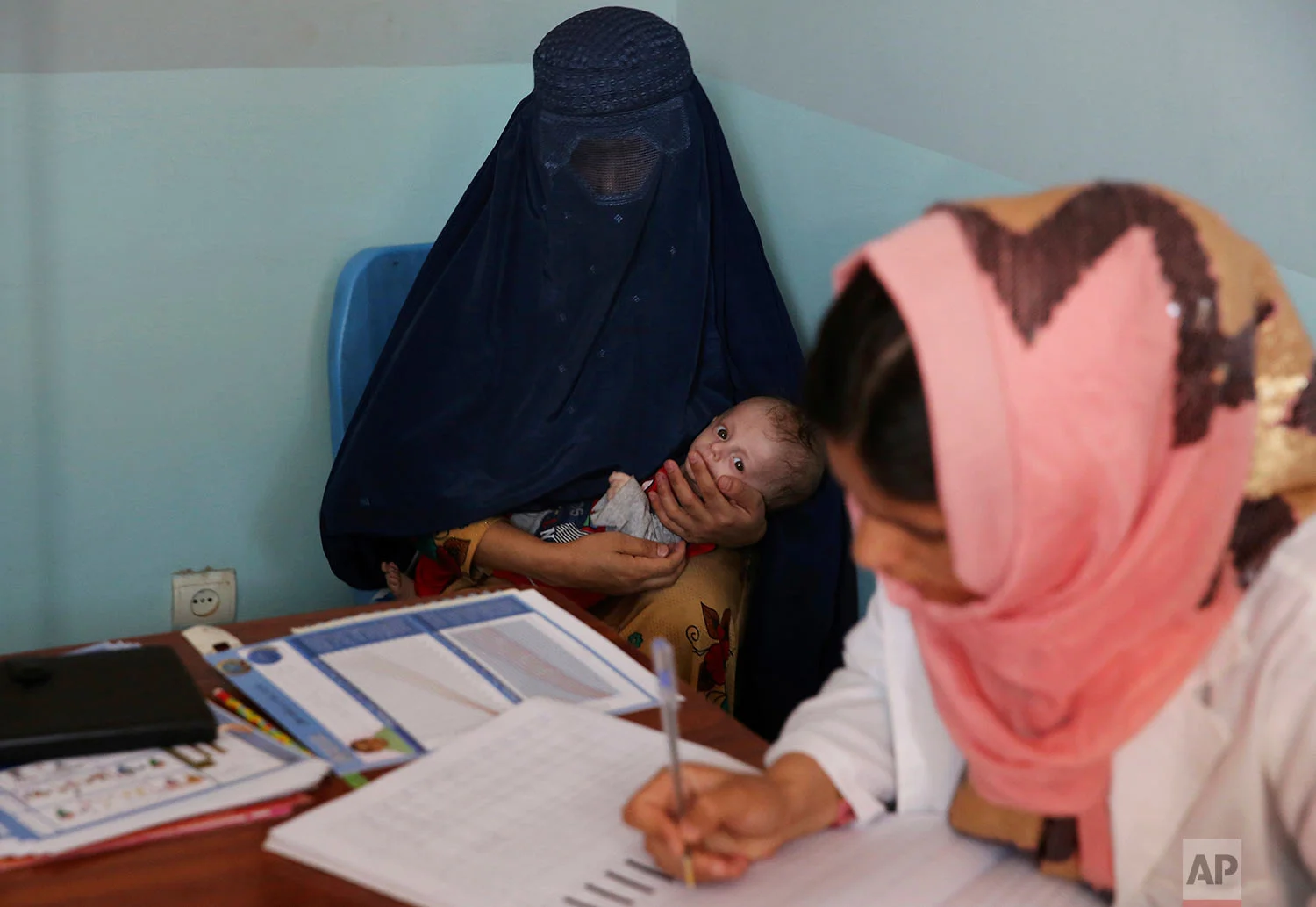 A woman holds her son, Abdullah, who is suffering from malnutrition as a doctor writes a prescription for him at a UNICEF clinic in Jabal Saraj north of Kabul, Afghanistan, Aug. 26, 2019. Days ago, he was at an emergency ward. (AP Photo/Rafiq Maqbool)