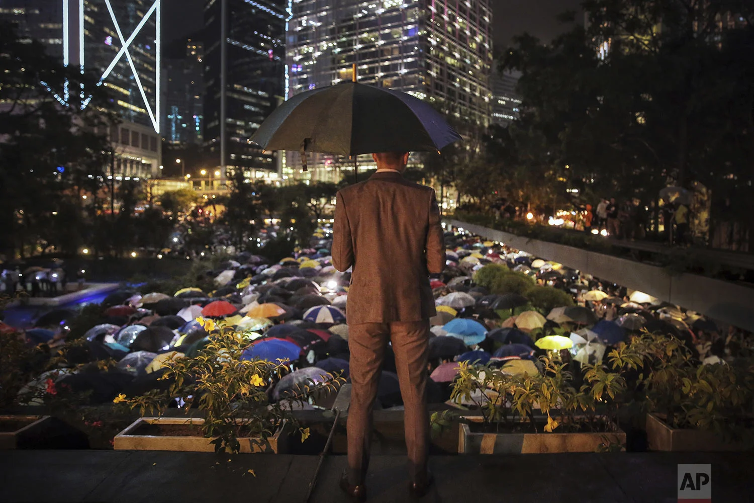 A man holding an umbrella looks at people with umbrellas gathered at Chater Garden to give support to the recent protests against the extradition bill, at the financial district in Hong Kong, Thursday, Aug, 1, 2019. (Elson Li/HK01 via AP)