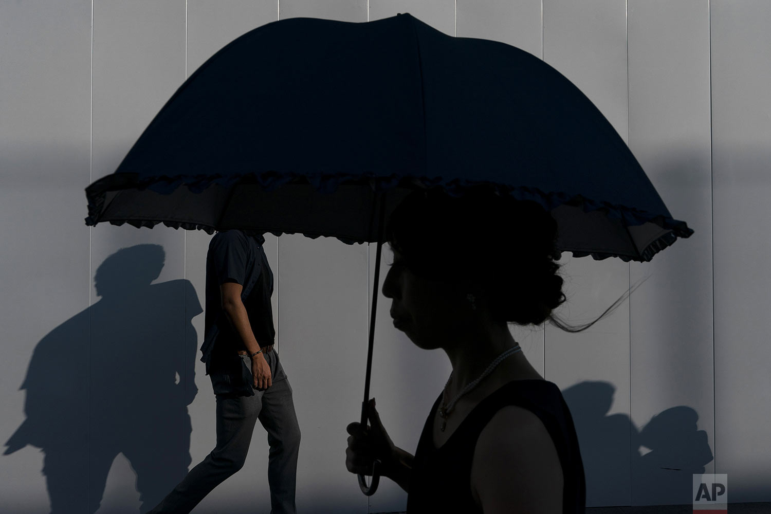  Pedestrians cast their shadows as they walk along a sidewalk Sunday, Aug. 11, 2019, in Tokyo's Roppongi district of Tokyo. (AP Photo/Jae C. Hong) 