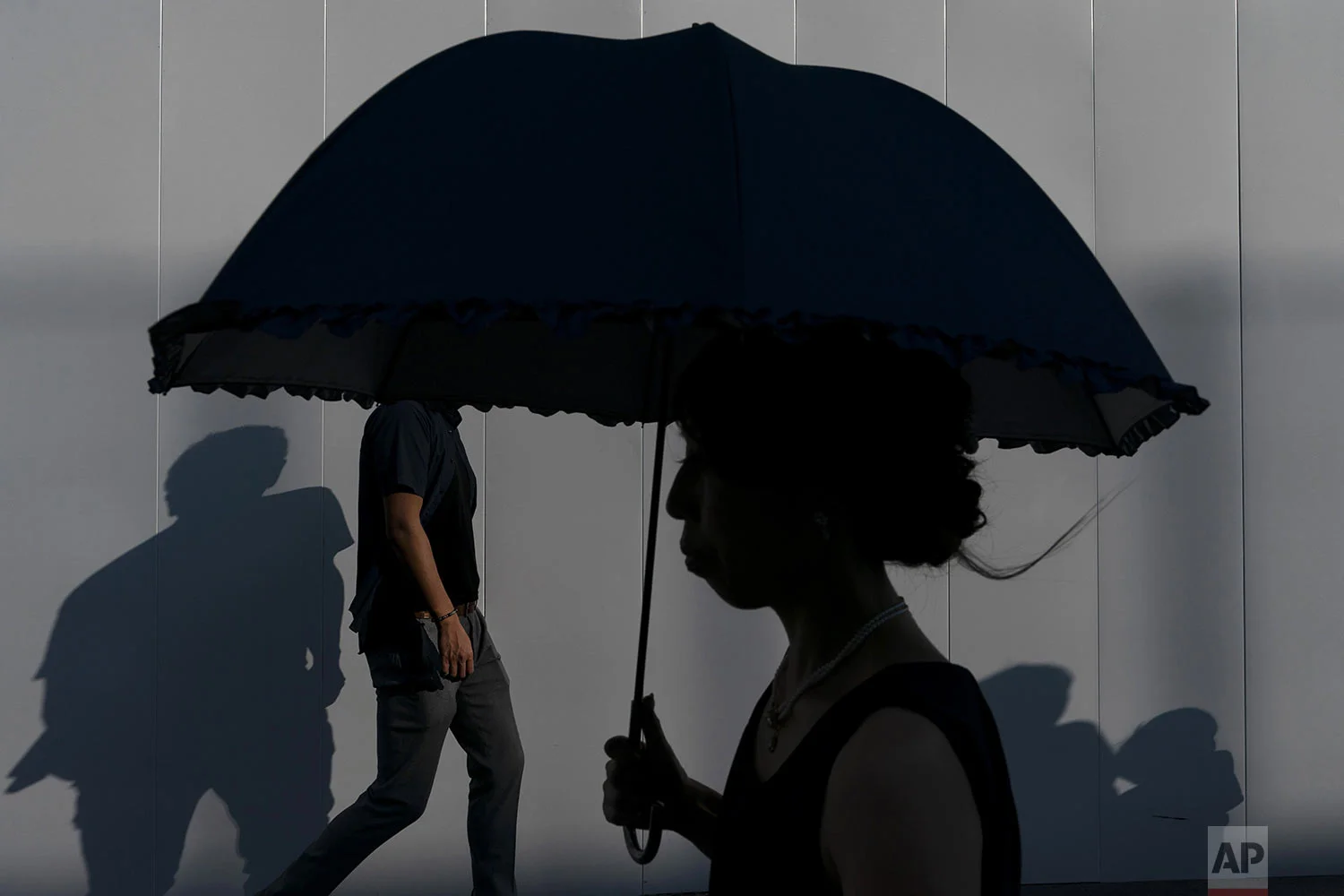 Pedestrians cast their shadows as they walk along a sidewalk Sunday, Aug. 11, 2019, in Tokyo's Roppongi district of Tokyo. (AP Photo/Jae C. Hong)