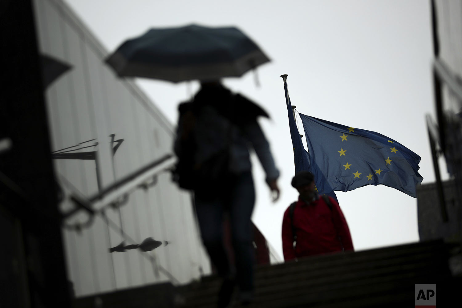 Passers-by shelter against the rain outside the EU headquarters in Brussels, Wednesday, Sept. 4, 2019. The European Union says so far it has received no proposals from the British government aimed at overcoming the impasse in Brexit talks. (AP Photo/Francisco Seco)