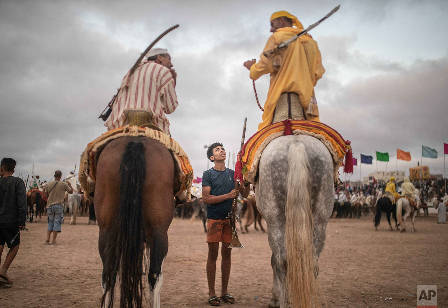 In this Thursday, July 25, 2019 photo, a boy hands a file to horseriders waiting for their turn to take part in an equestrian show known as Fantasia or Tabourida, in the coastal town of El Jadida, Morocco. (AP Photo/Mosa'ab Elshamy)