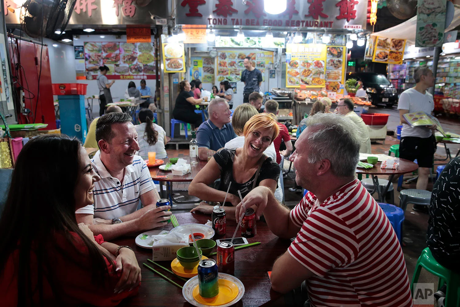 A group of British tourists share a laugh around a dinner table at Temple Street Night Market in Hong Kong, Sept. 2, 2019. (AP Photo/Jae C. Hong)