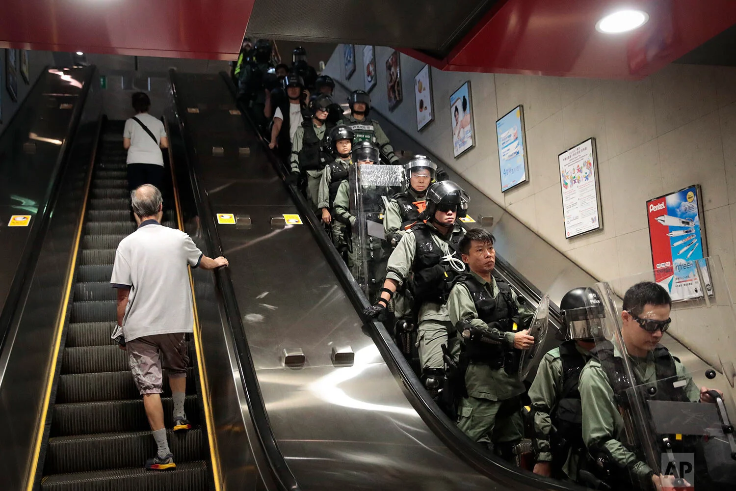 Two commuters ride an escalator at a train station past police officers in riot gear deployed to arrest protesters in Hong Kong, Sept. 2, 2019. (AP Photo/Jae C. Hong)