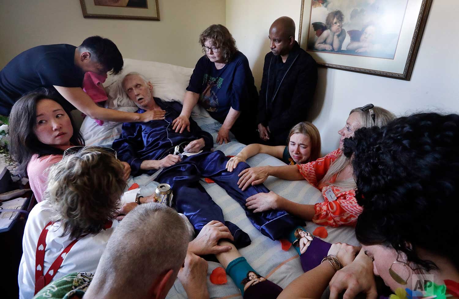  In this May 10, 2019, photo, Robert Fuller lies unconscious after plunging prescribed drugs to end his life into his feeding tube as his husband, Reese Baxter, upper left, and friends lay hands on him, in Seattle. Earlier in the day, Fuller had the 