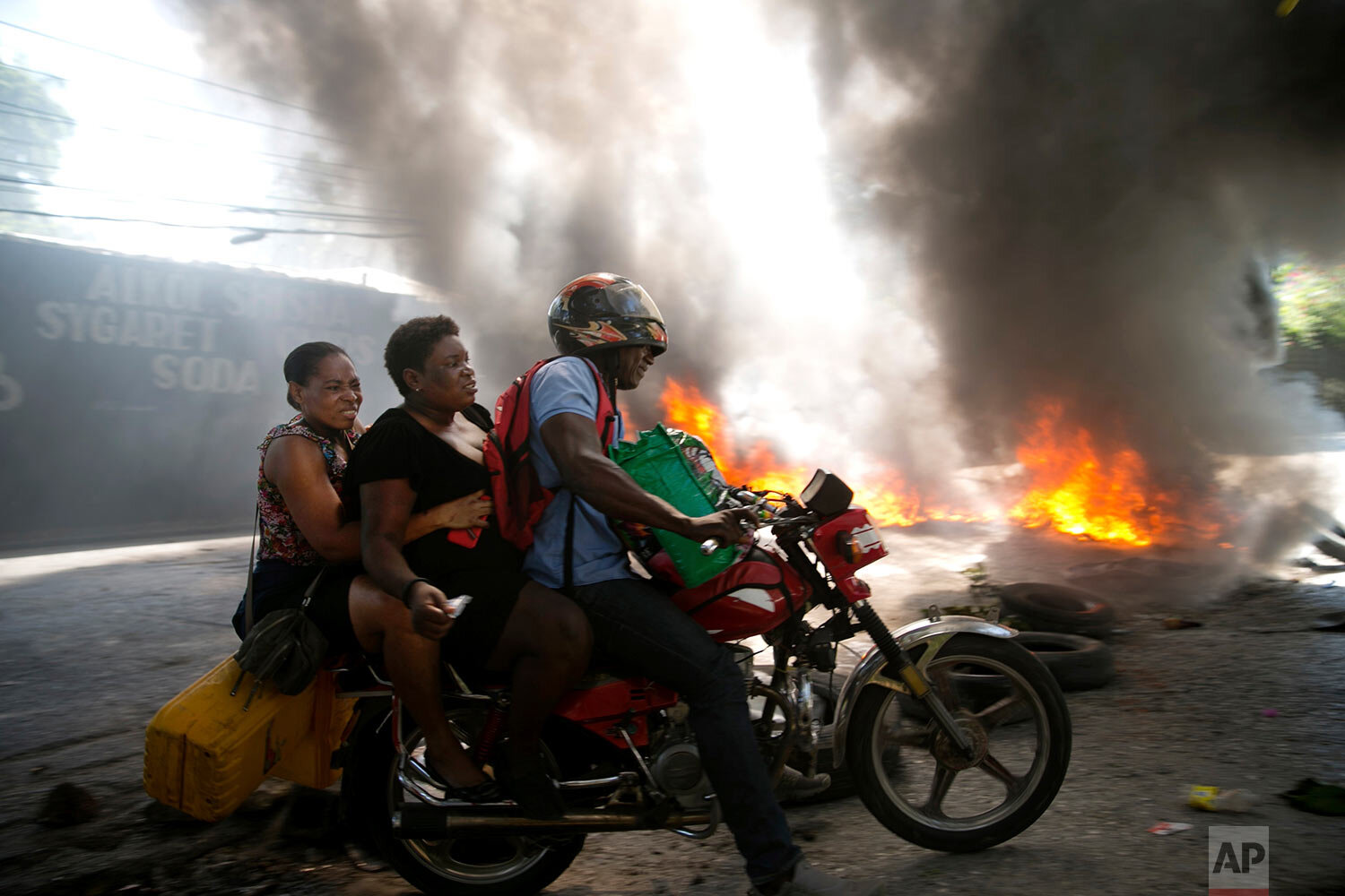  A moto-taxi driver takes two women around a burning barricade set up by people protesting fuel shortages in Petion-ville, Haiti, Sunday, Sept. 15, 2019. Gas stations have been reducing their operating hours over the past weeks, and the majority were