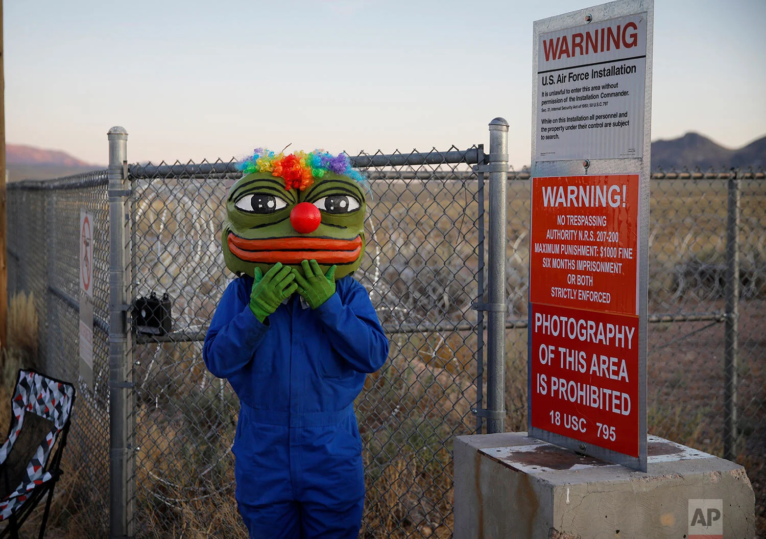 Martin Custodio wears a Pepe mask while standing near razor wire at an entrance to the Nevada Test and Training Range near Area 51, Friday, Sept. 20, 2019, near Rachel, Nev. (AP Photo/John Locher)