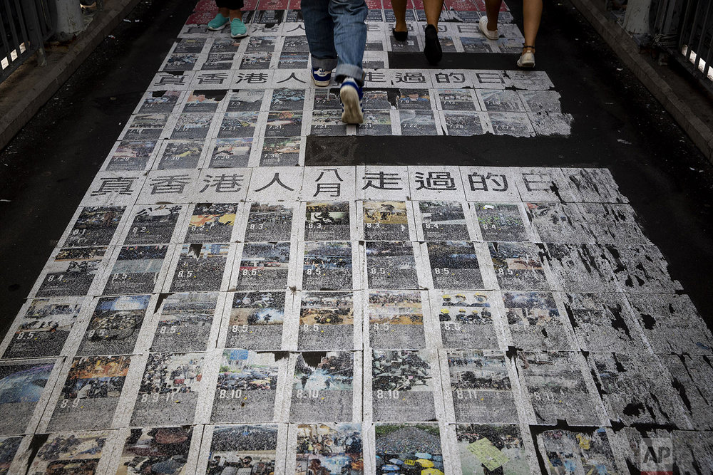  People walk on photos showing the recent protests with the words "The days the Hong Kong people have passed" at a pedestrian overhead bridge in Hong Kong, Wednesday, Sept. 25, 2019. (AP Photo/Vincent Thian) 