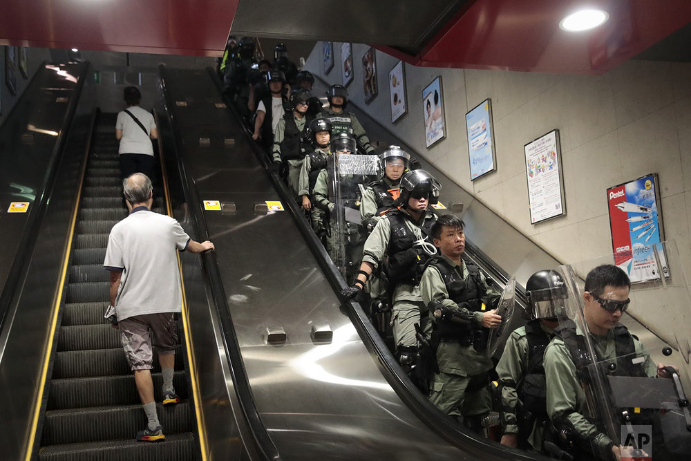  Two commuters ride an escalator at a train station past police officers in riot gear deployed to arrest protesters in Hong Kong, Monday, Sept. 2, 2019. (AP Photo/Jae C. Hong) 