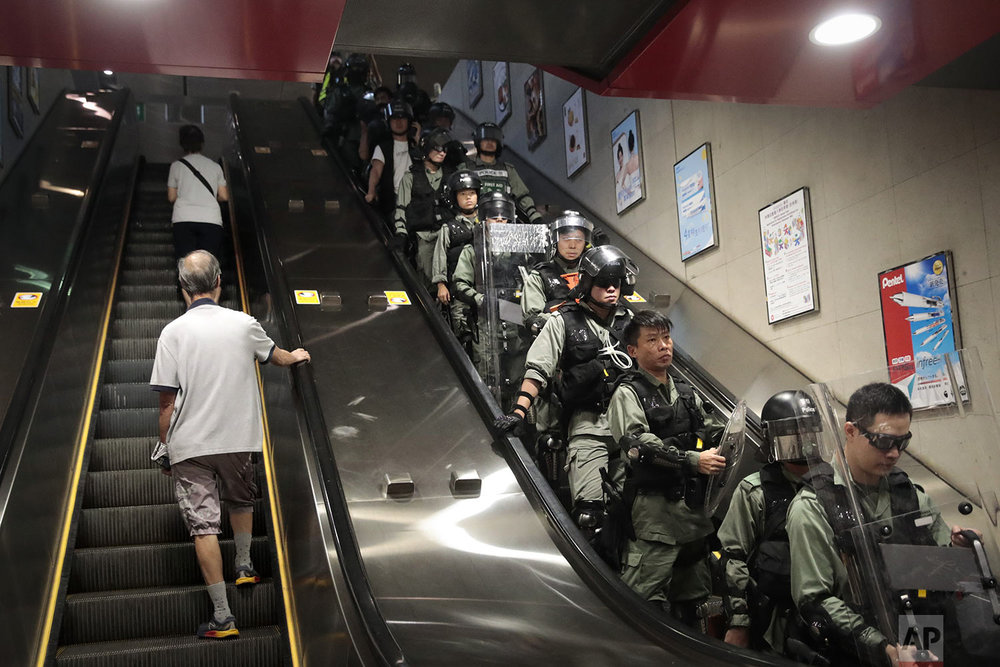 Two commuters ride an escalator at a train station past police officers in riot gear deployed to arrest protesters in Hong Kong, Monday, Sept. 2, 2019. (AP Photo/Jae C. Hong)