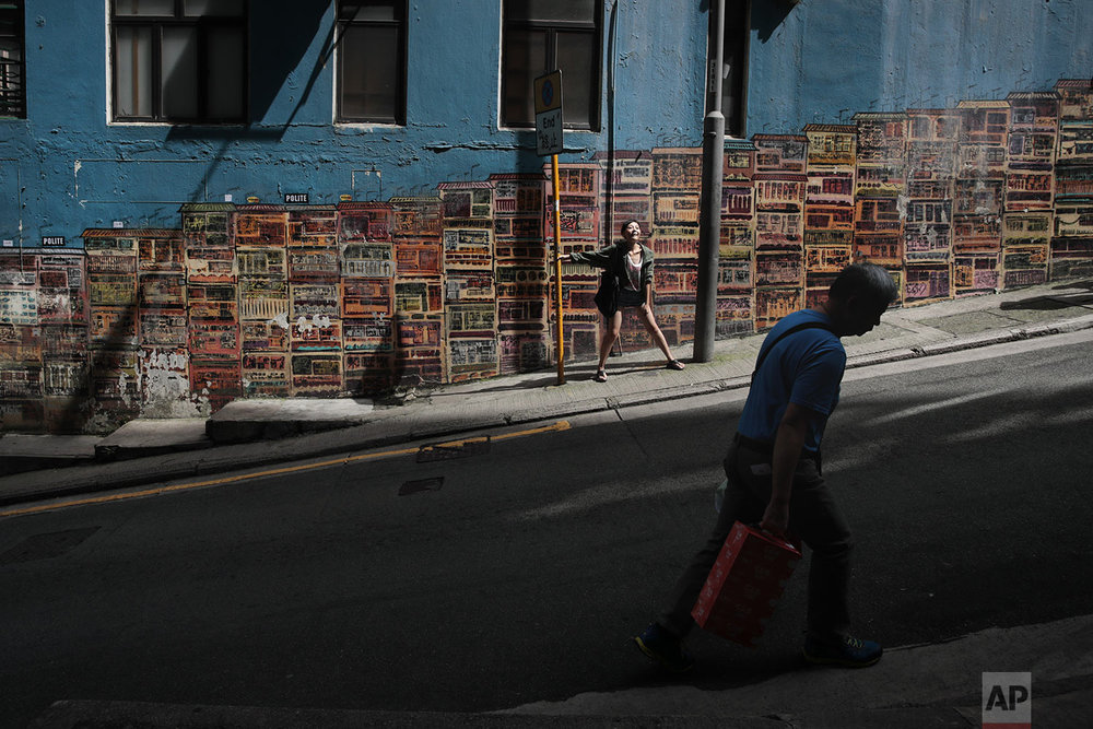 A tourist poses for photos in front of a popular mural by artist Alex Croft in the SoHo district of Hong Kong, Tuesday, Sept. 3, 2019. (AP Photo/Jae C. Hong)