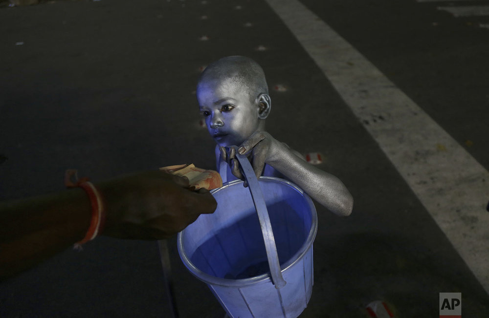A young boy with his body painted and dressed as Mahatma Gandhi seek alms at a traffic intersection in Hyderabad, India, Tuesday, Sept.10, 2019. (AP Photo/Mahesh Kumar A.)