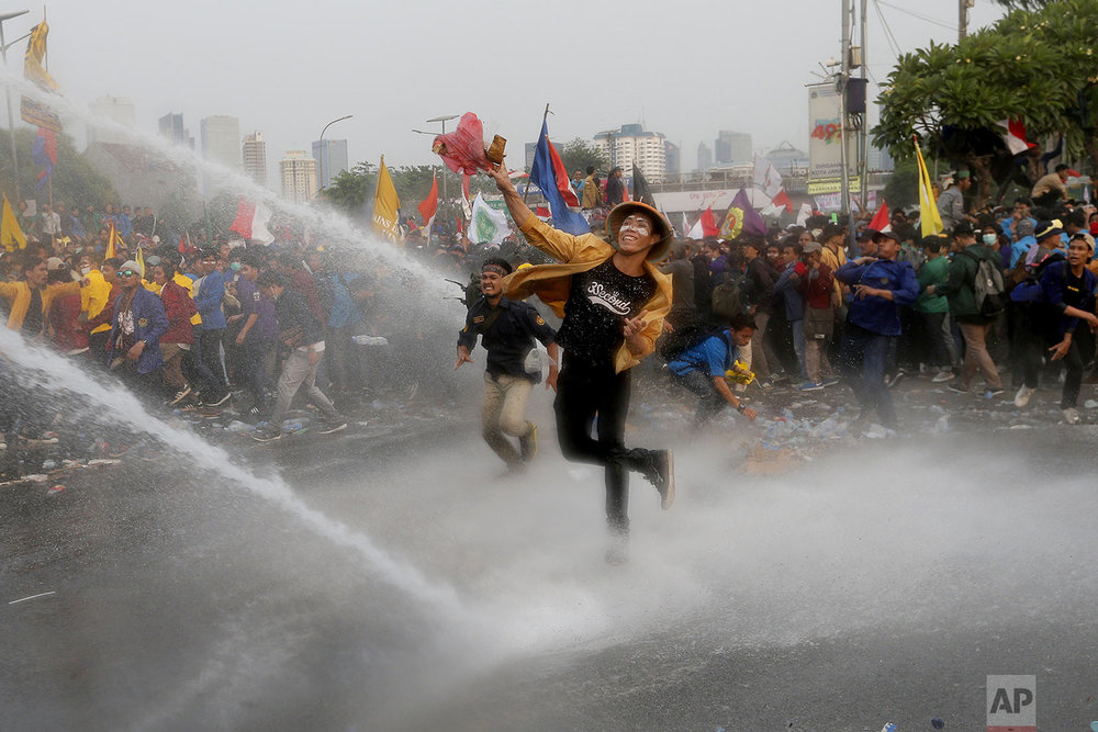 Student protesters hurl objects as they are sprayed by a police water cannon truck during a protest outside the parliament in Jakarta, Indonesia, Tuesday, Sept. 24, 2019. (AP Photo/Tatan Syuflana)
