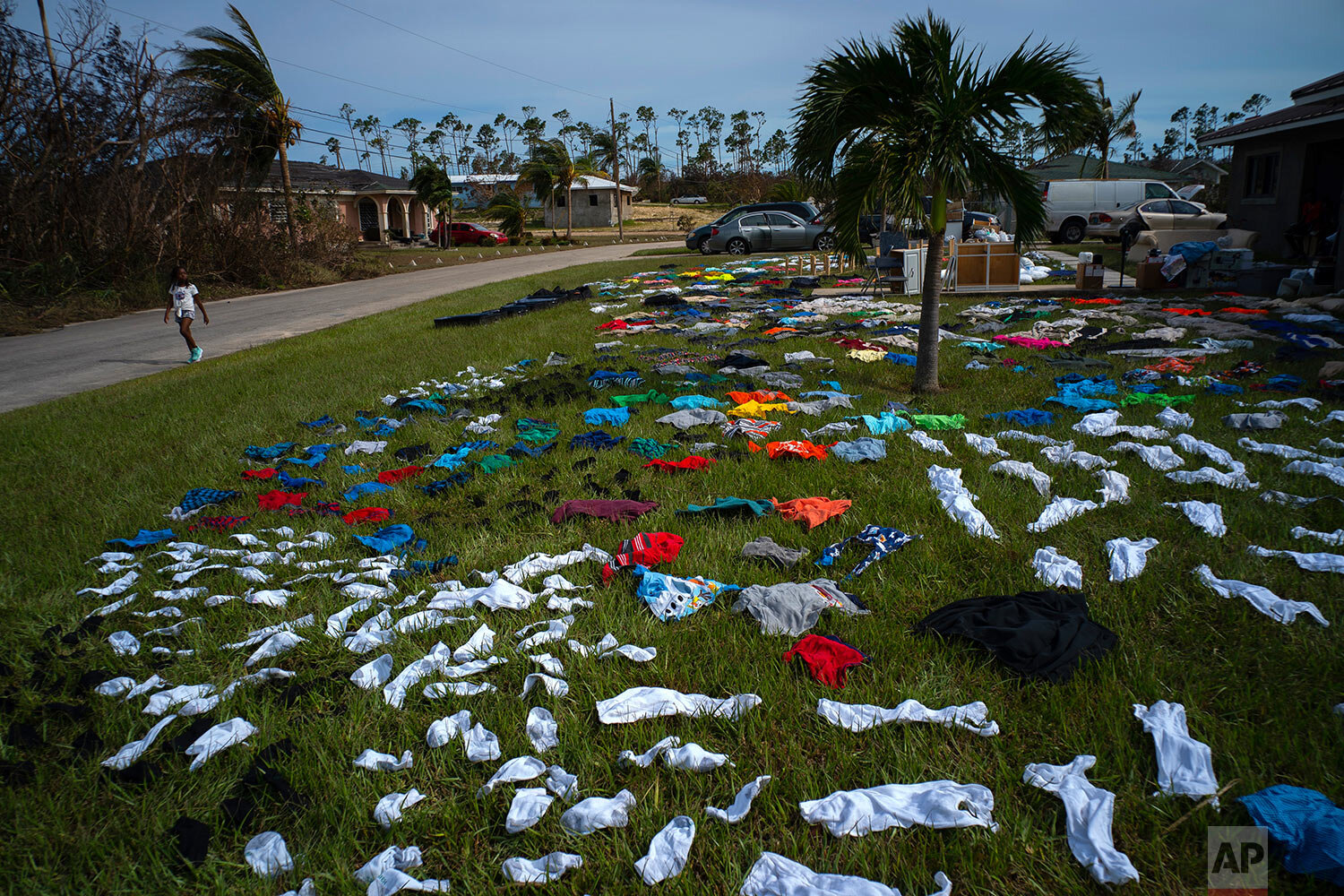 A child walks past clothes laid out to dry on a field in the aftermath of Hurricane Dorian, in the Arden Forest neighborhood of Freeport, Bahamas, Wednesday, Sept. 4, 2019. (AP Photo/Ramon Espinosa)
