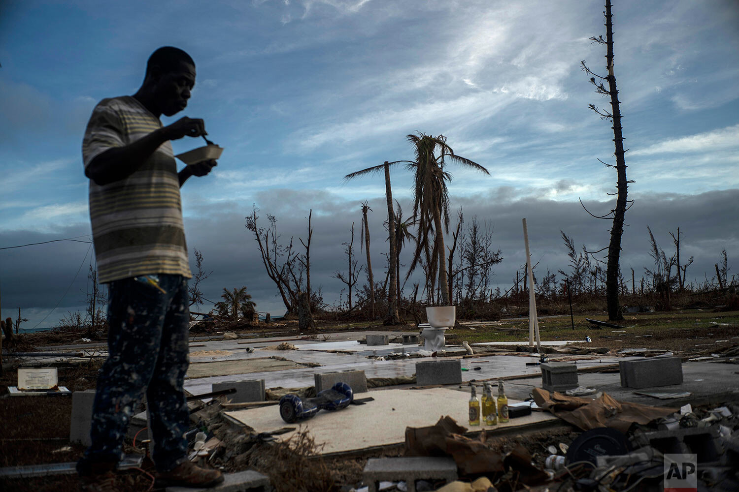 Jeffrey Roberts, 49, eats a plate of food while searching through the rubble of his relatives' home which was destroyed by Hurricane Dorian in Pelican Point, Grand Bahama, Bahamas, Saturday, Sept. 14, 2019. (AP Photo/Ramon Espinosa)